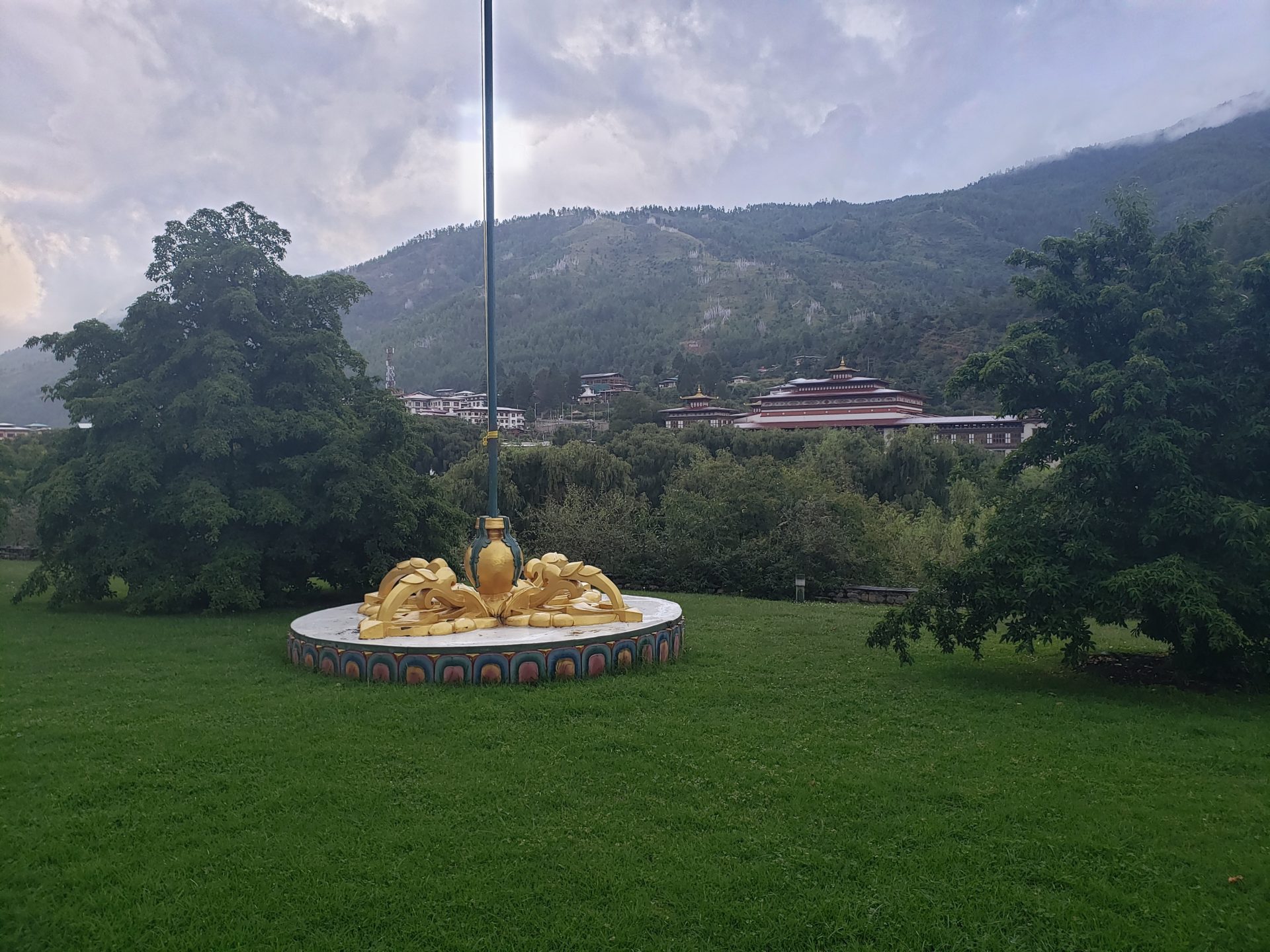 a statue on a pedestal in a grassy area with trees and mountains in the background