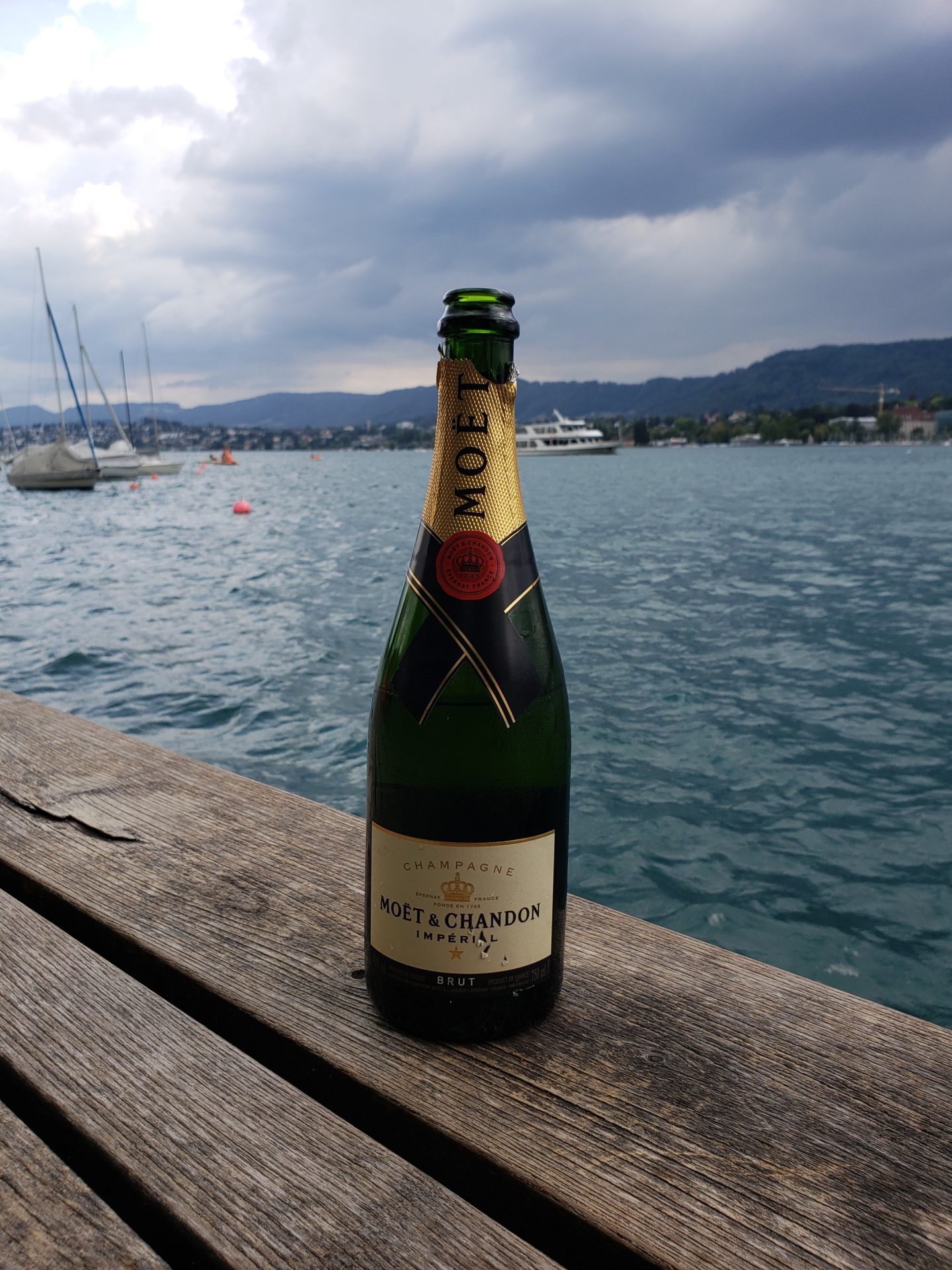a bottle of champagne on a wood surface with water in the background