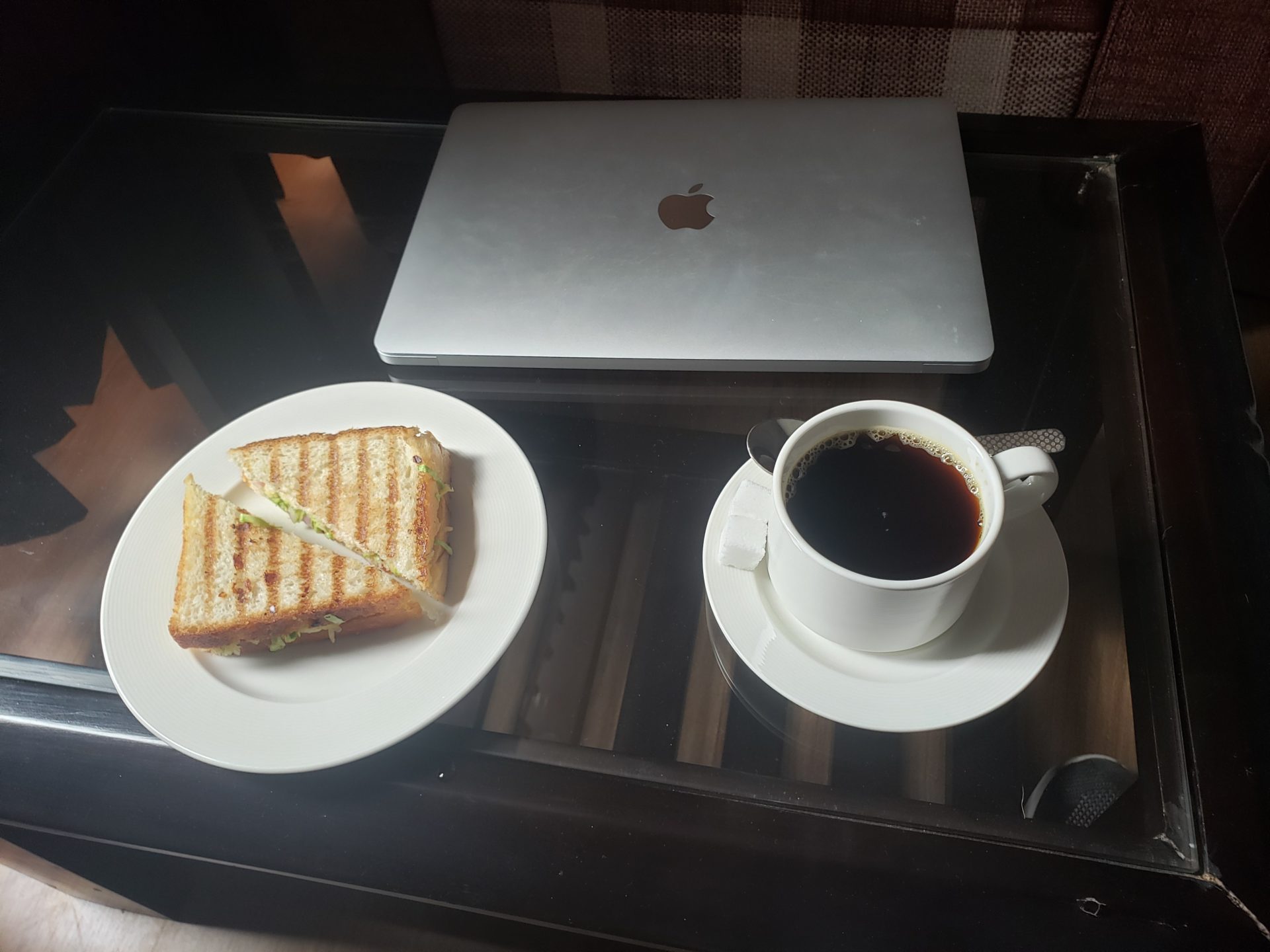 a plate of sandwich and a cup of coffee on a glass table