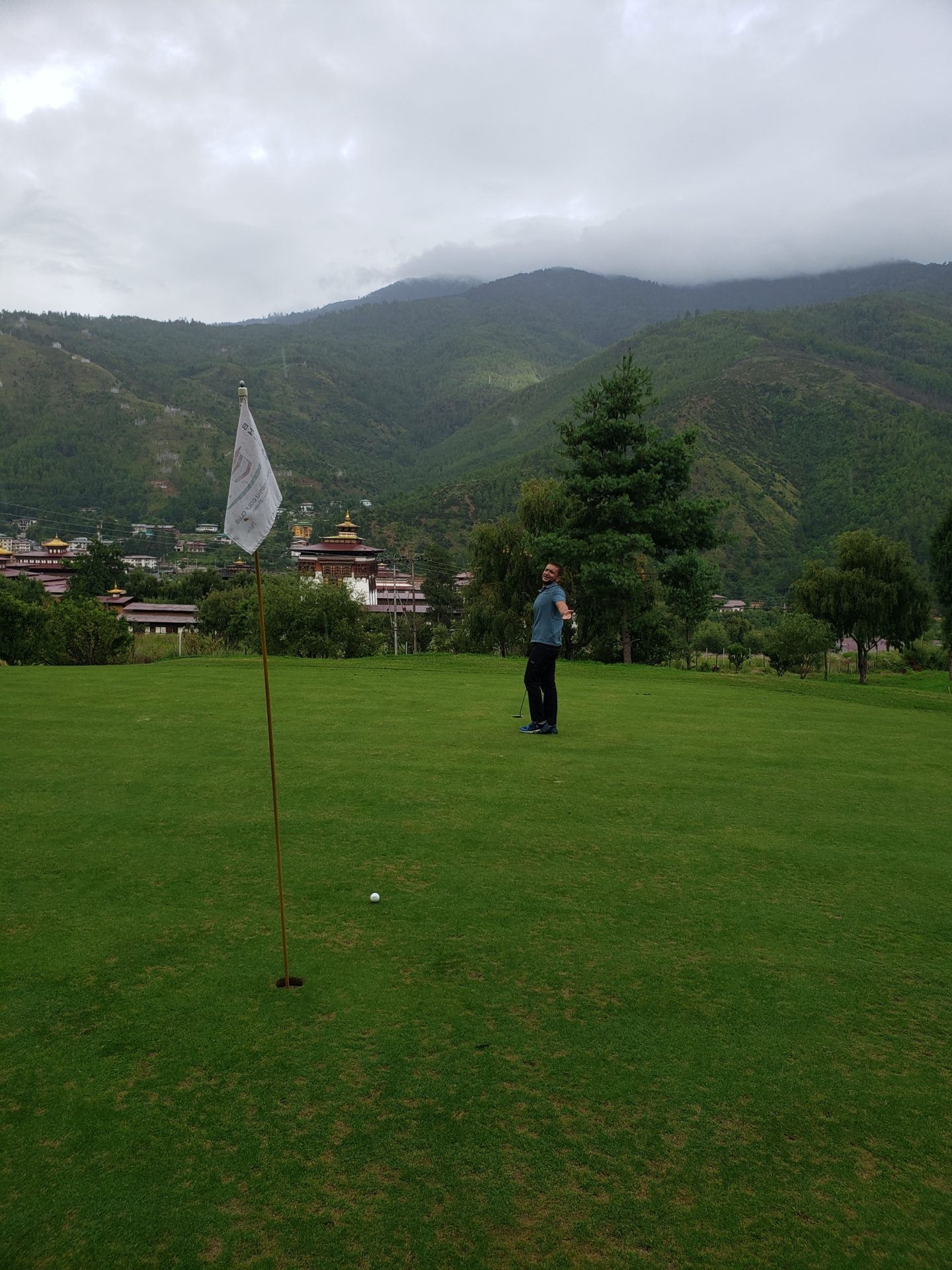 a man standing on a golf course with a flag in front of mountains