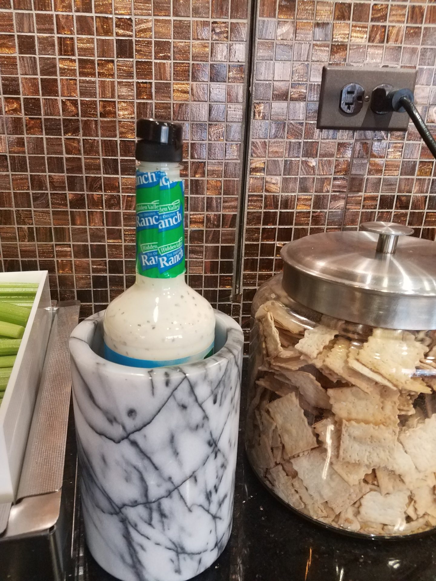 a bottle of sauce in a marble container next to a jar of crackers