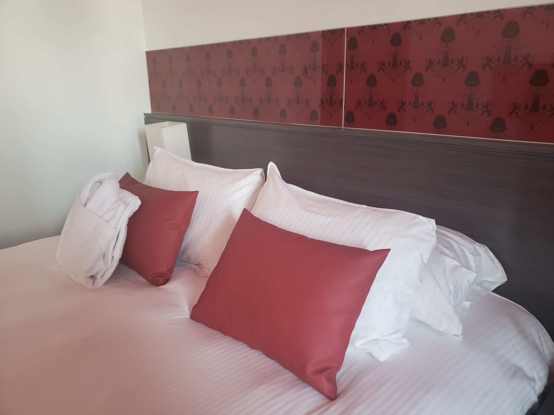 a bed with red pillows and a white robe