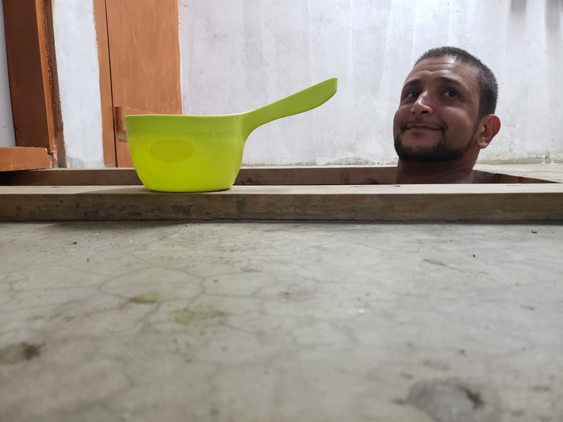 a man looking out of a hole with a green ladle