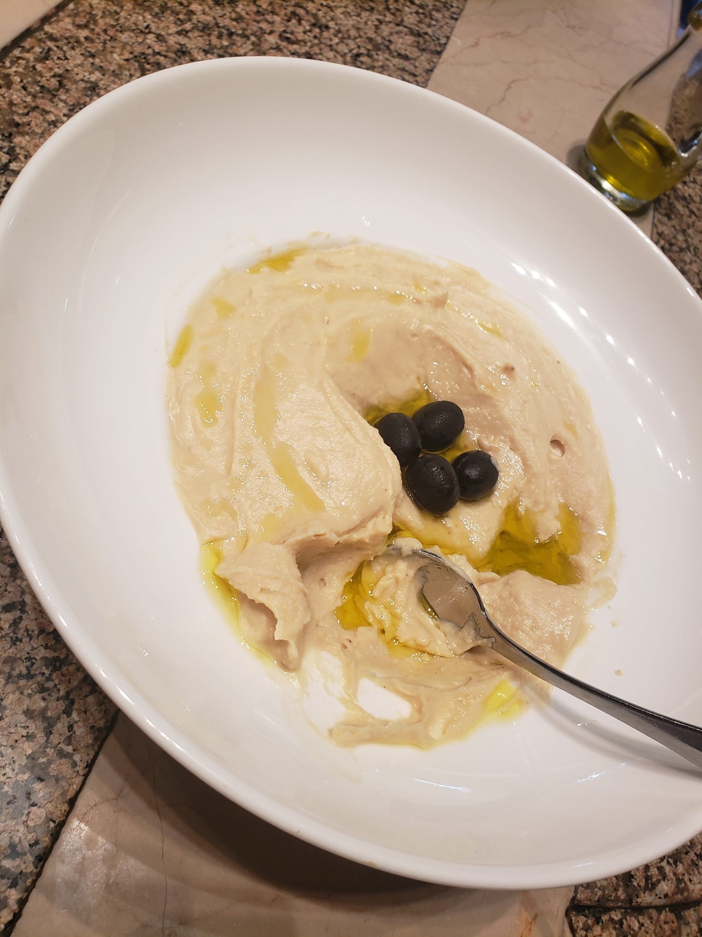 a bowl of hummus with olives and a spoon