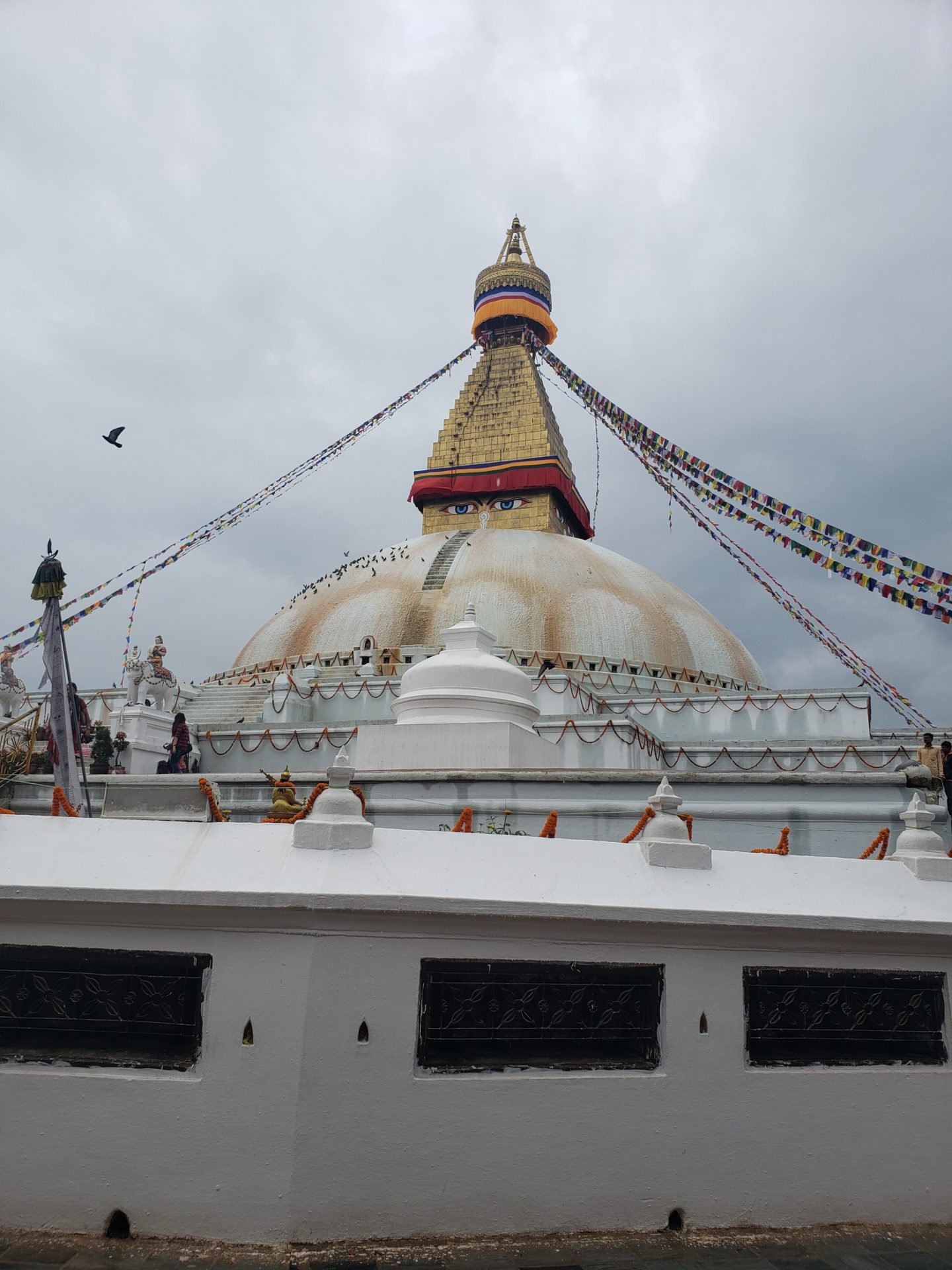 a white building with a dome and flags with Boudhanath in the background