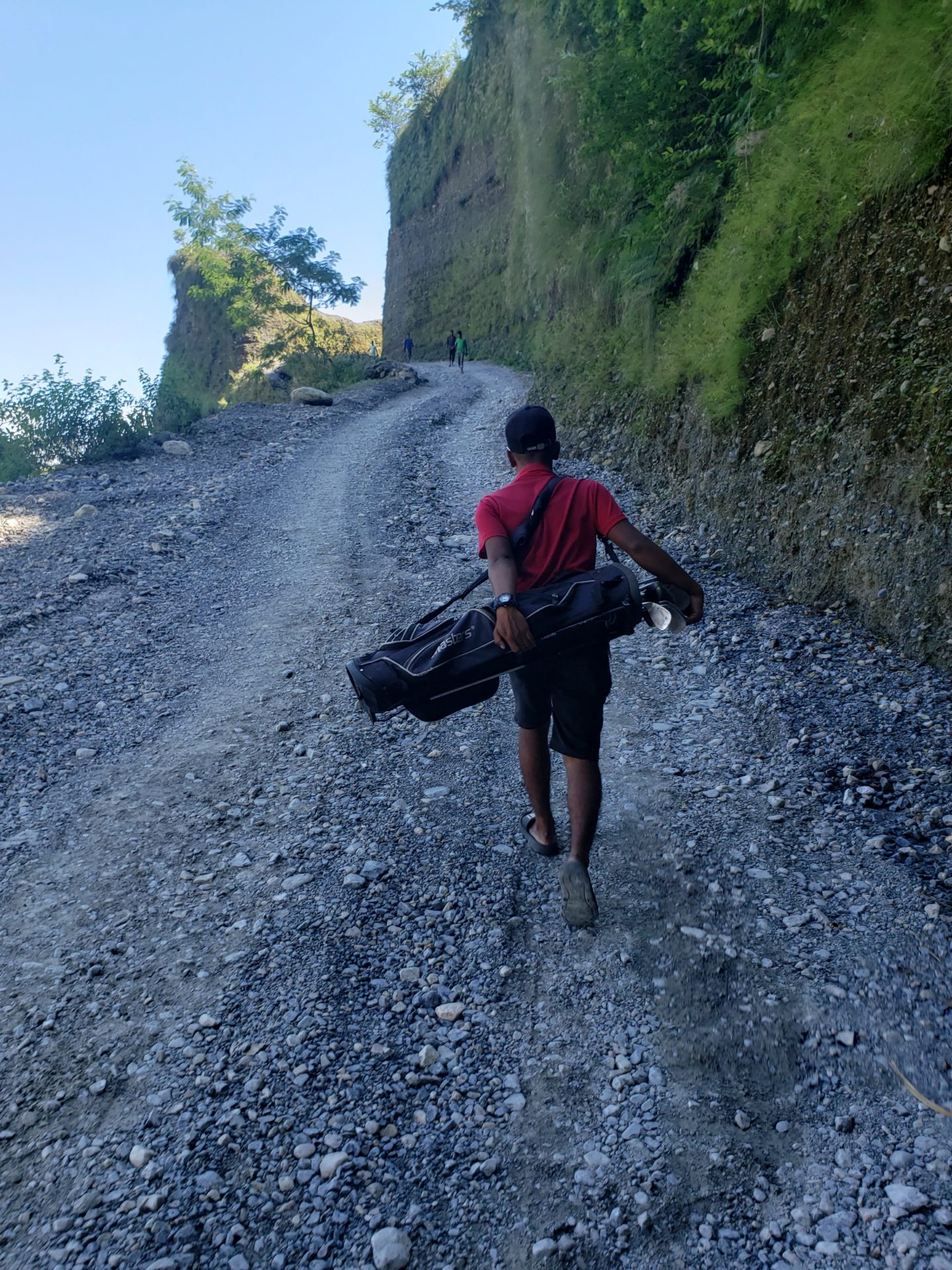 a man carrying golf bags on a rocky road