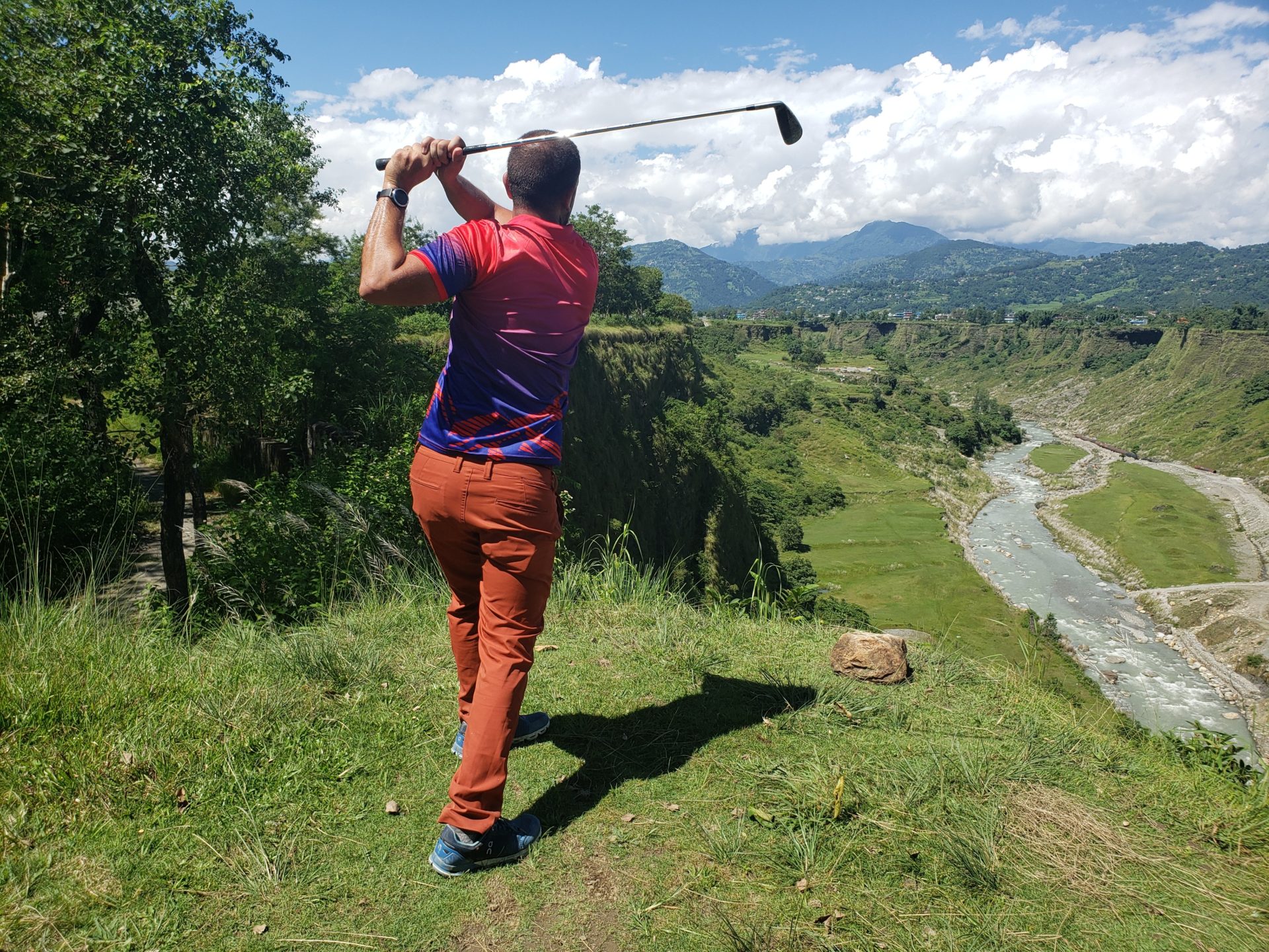 a man swinging a golf club on a grassy hill