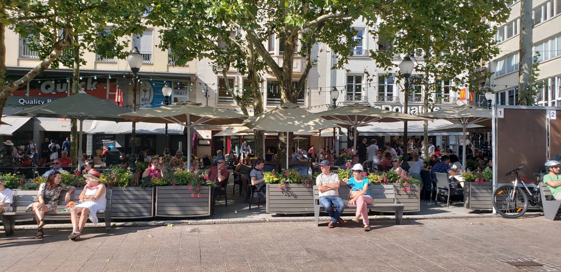 people sitting on benches in a courtyard with umbrellas and people around them