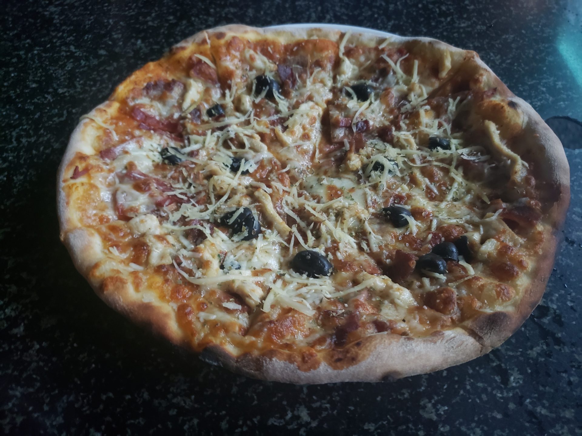 a pizza with olives and cheese on a black counter