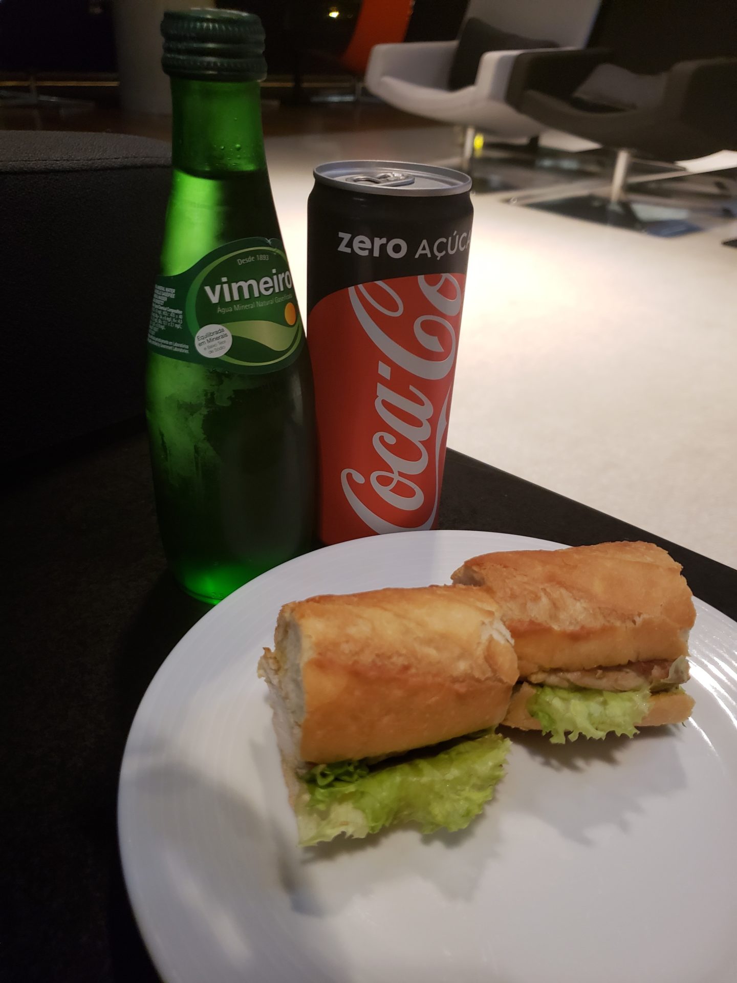 a sandwich on a plate next to a soda and a bottle