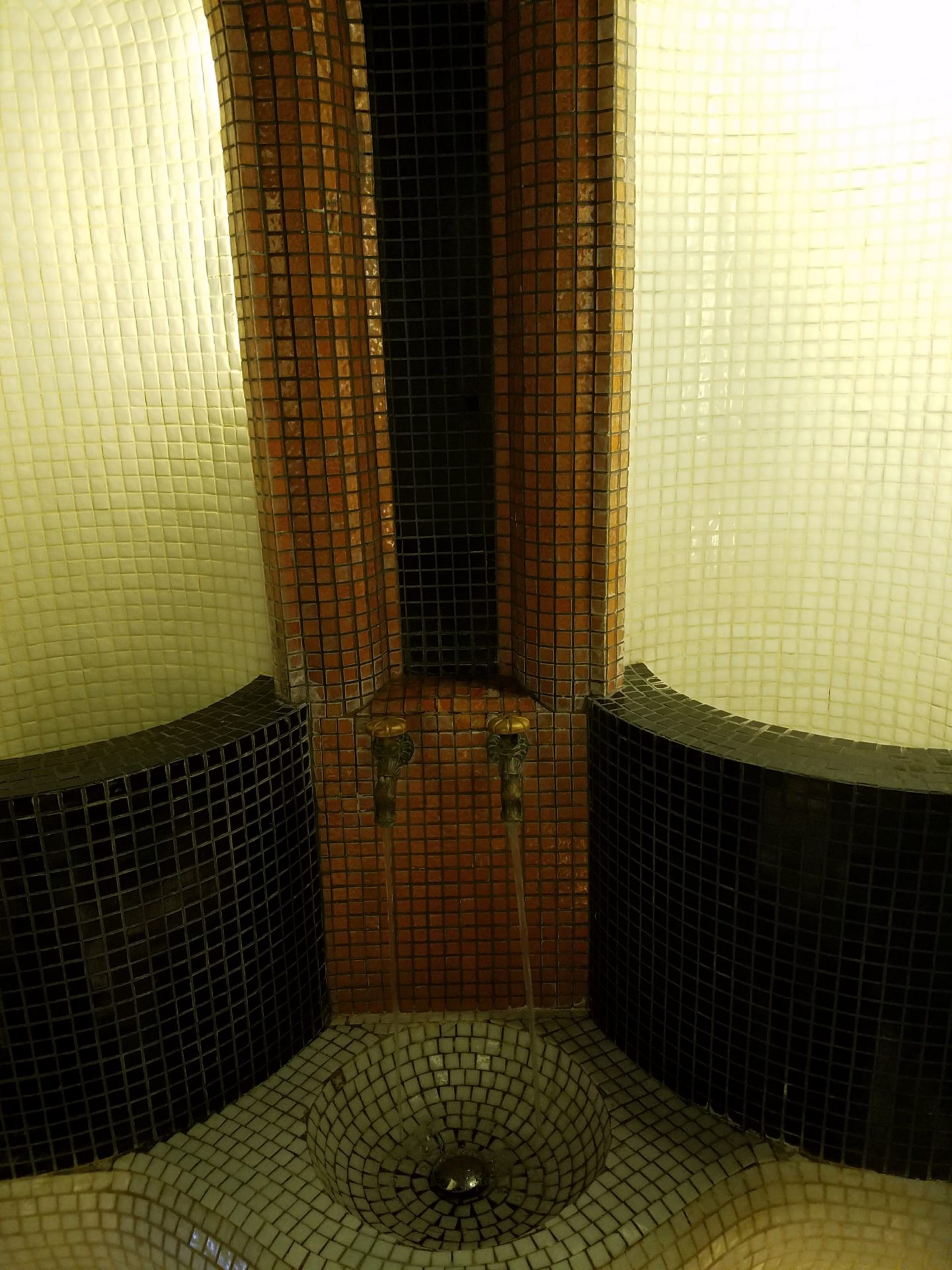 a urinal with a black and white tiled wall