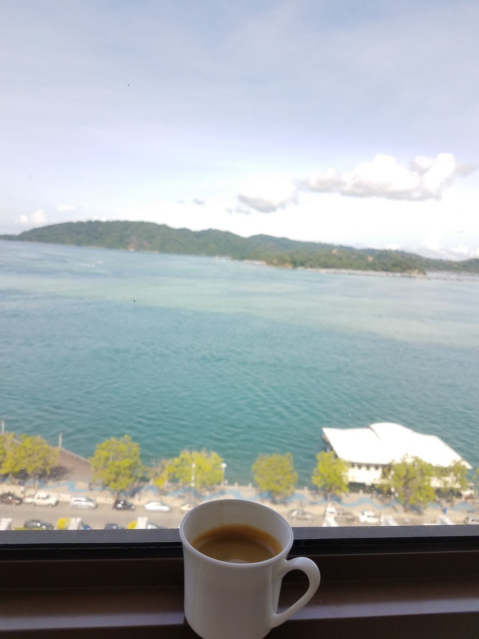 a cup of coffee on a window sill overlooking a body of water