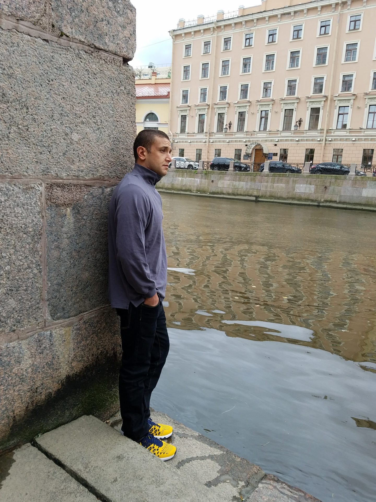 a man leaning against a wall next to a body of water