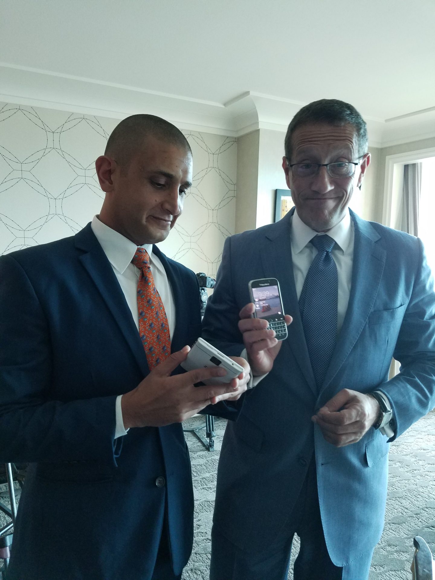 two men in suits holding a phone and a game controller