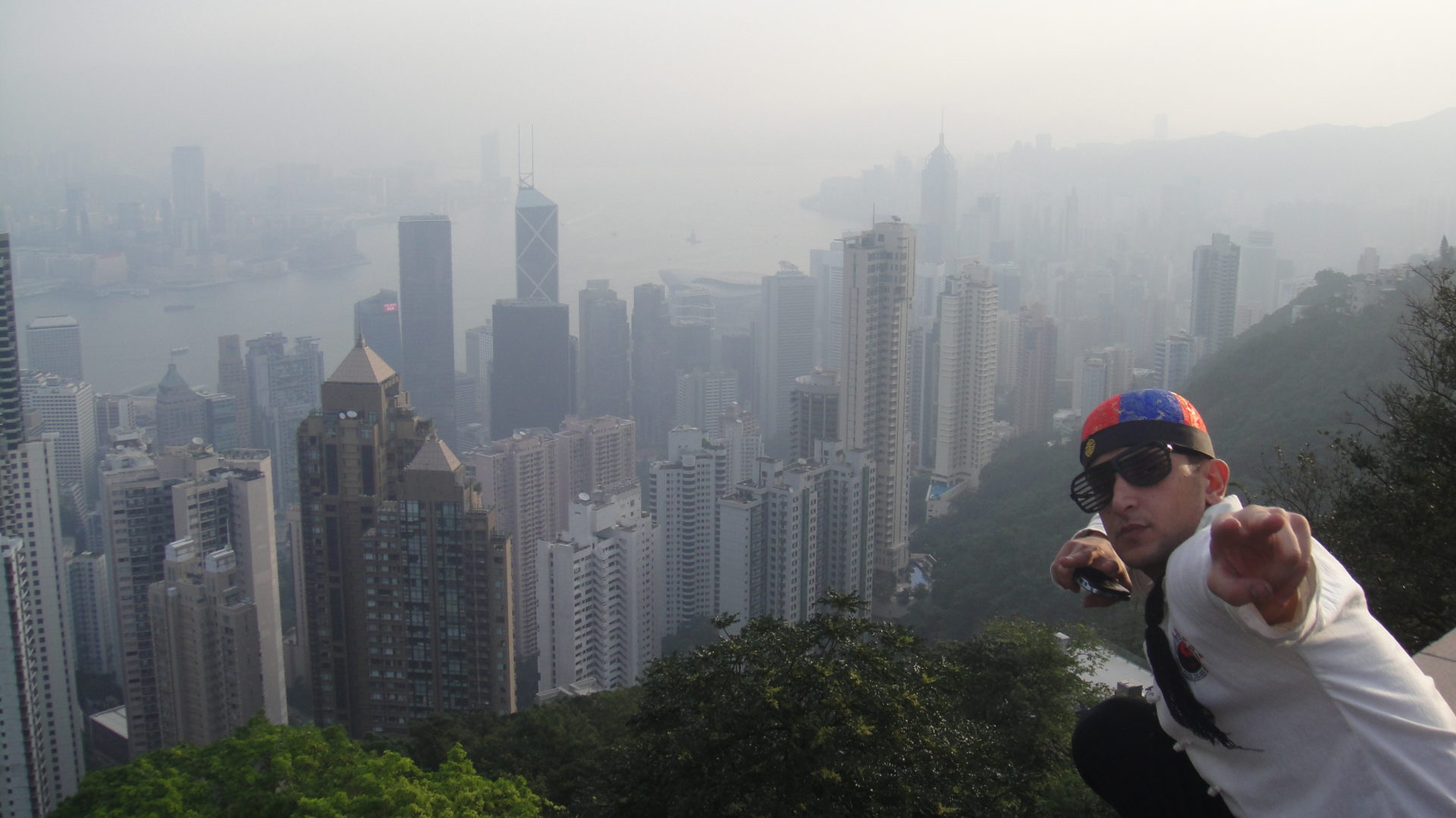 a man standing on a ledge with Victoria Peak in the background