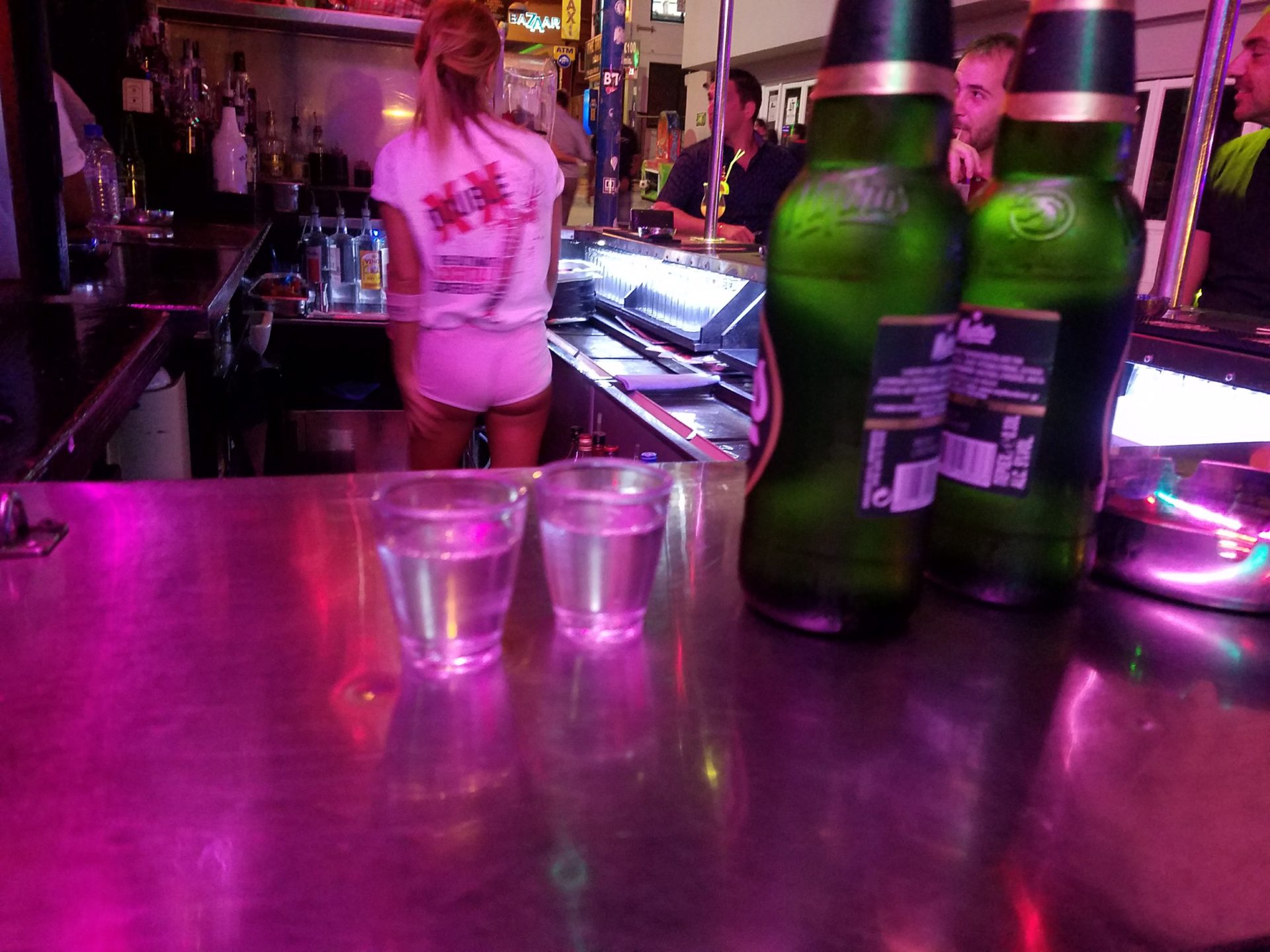 a woman standing at a bar with two glasses of liquid