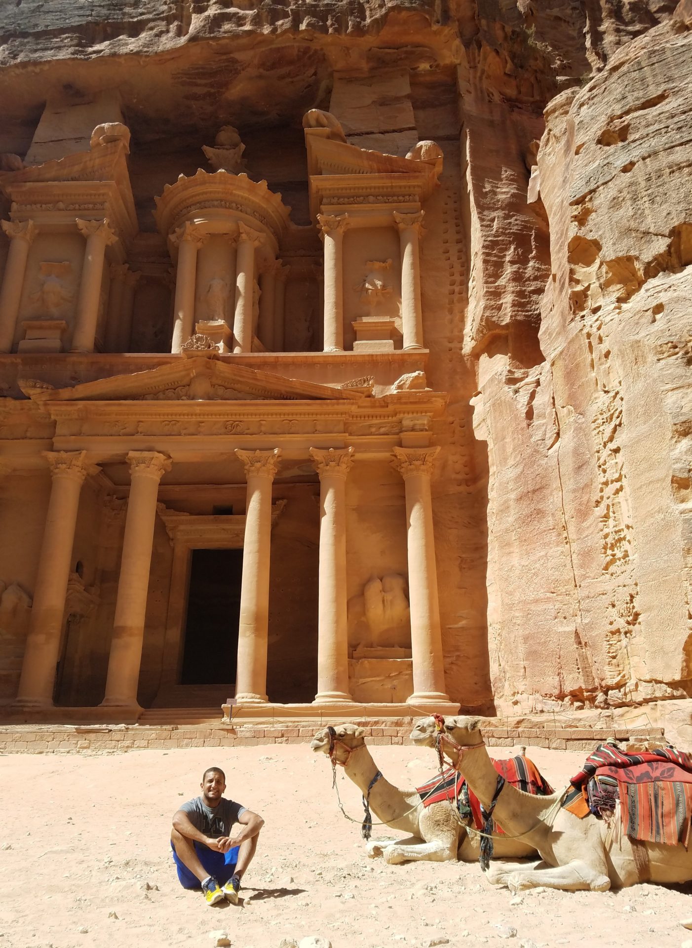 a man sitting in front of Petra with camels