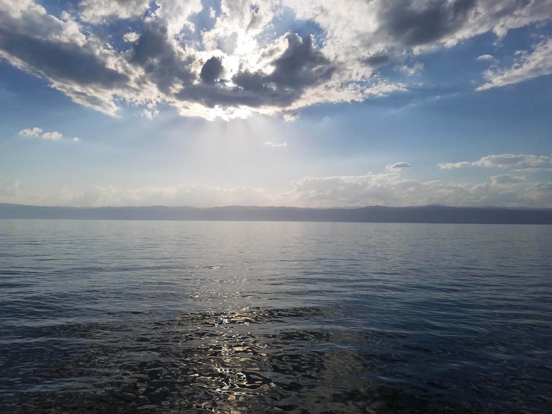 a body of water with clouds and sun shining through the clouds