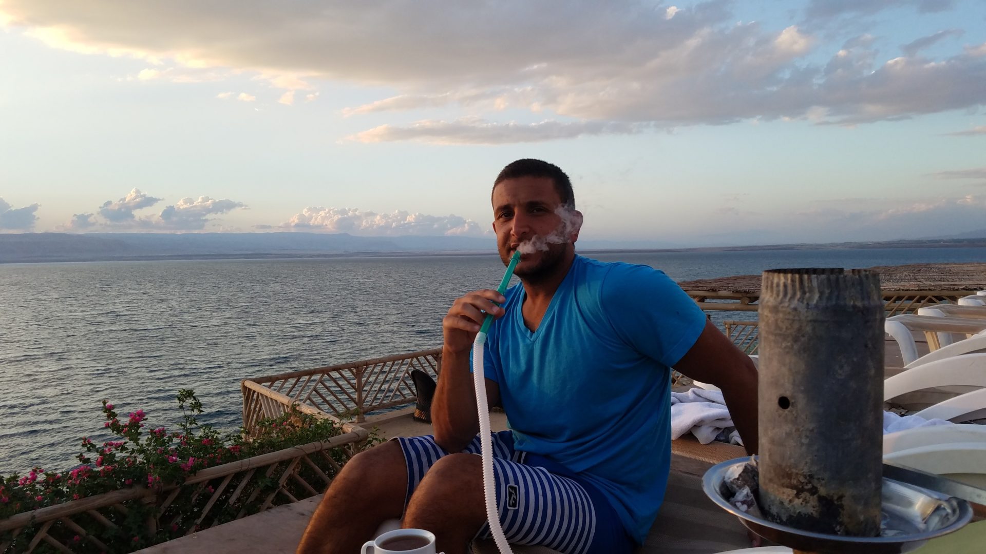 a man smoking a hookah on a deck overlooking a body of water