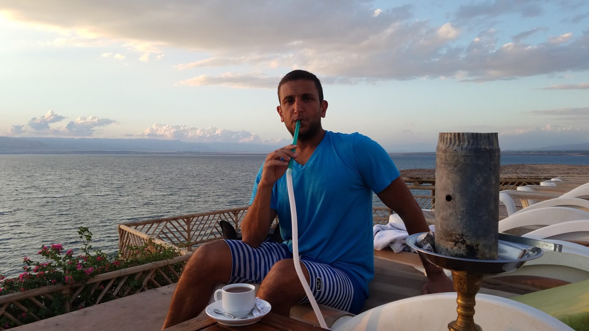 a man sitting on a deck with a hookah and a cup of tea