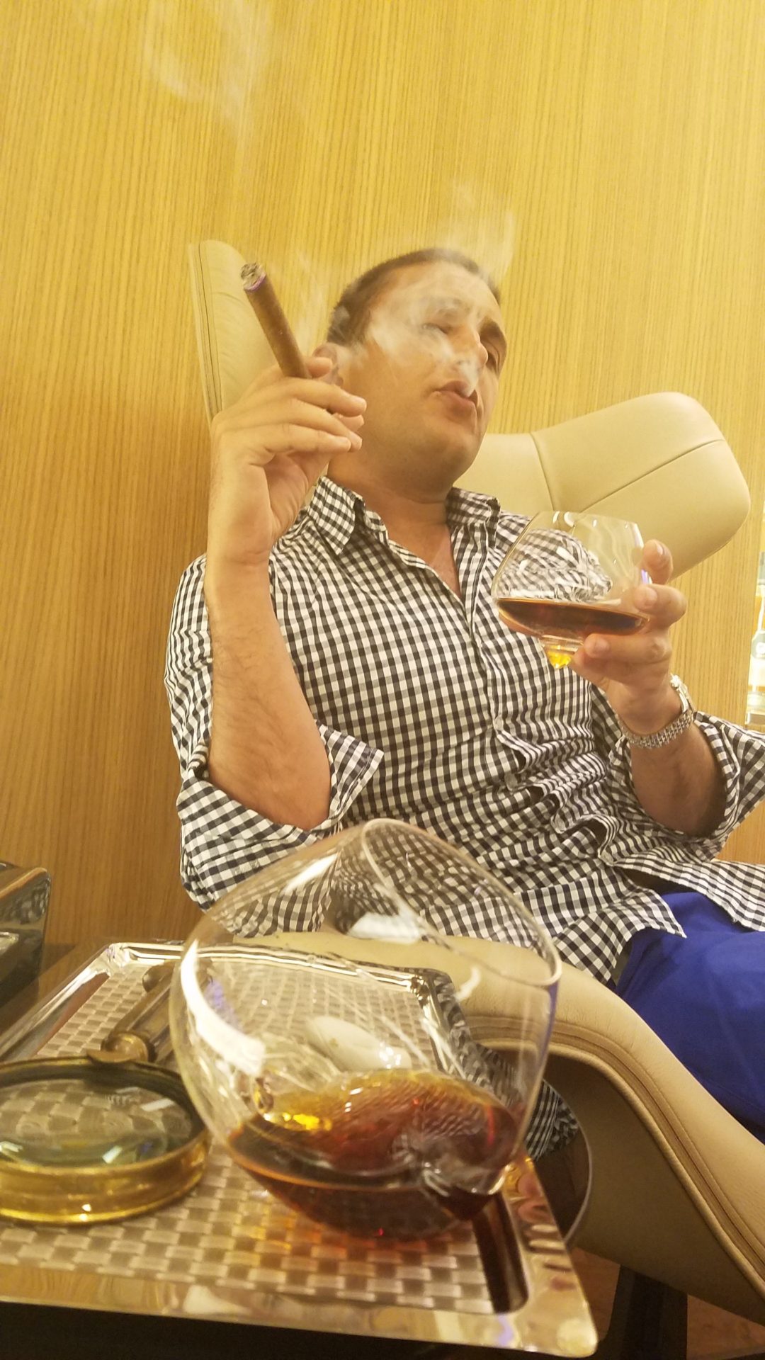 a man sitting in a chair smoking a cigar and drinking alcohol