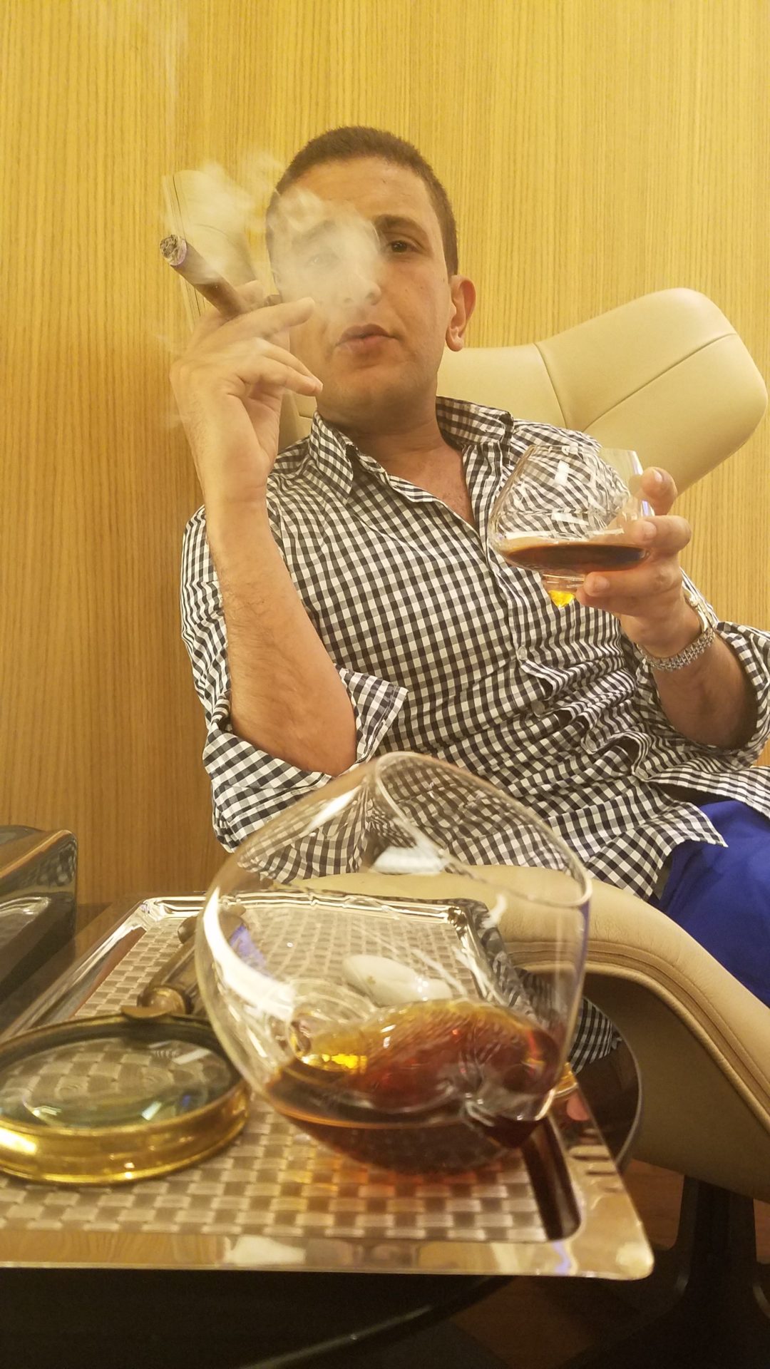 a man sitting in a chair smoking a cigar and drinking alcohol
