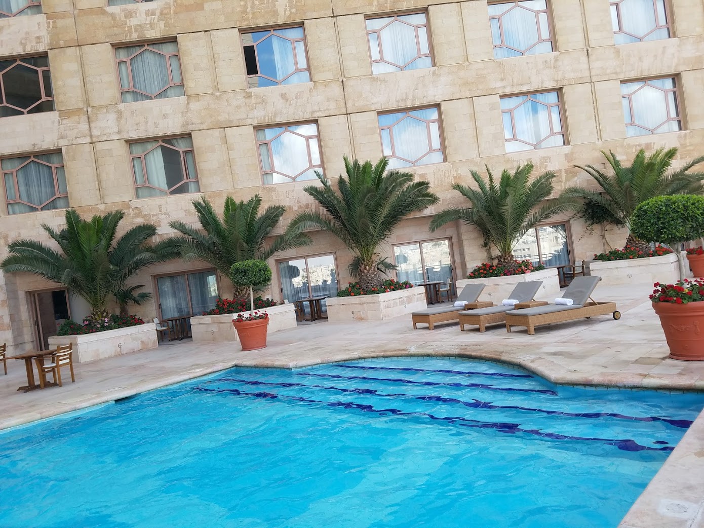 a pool with lounge chairs and palm trees in front of a building