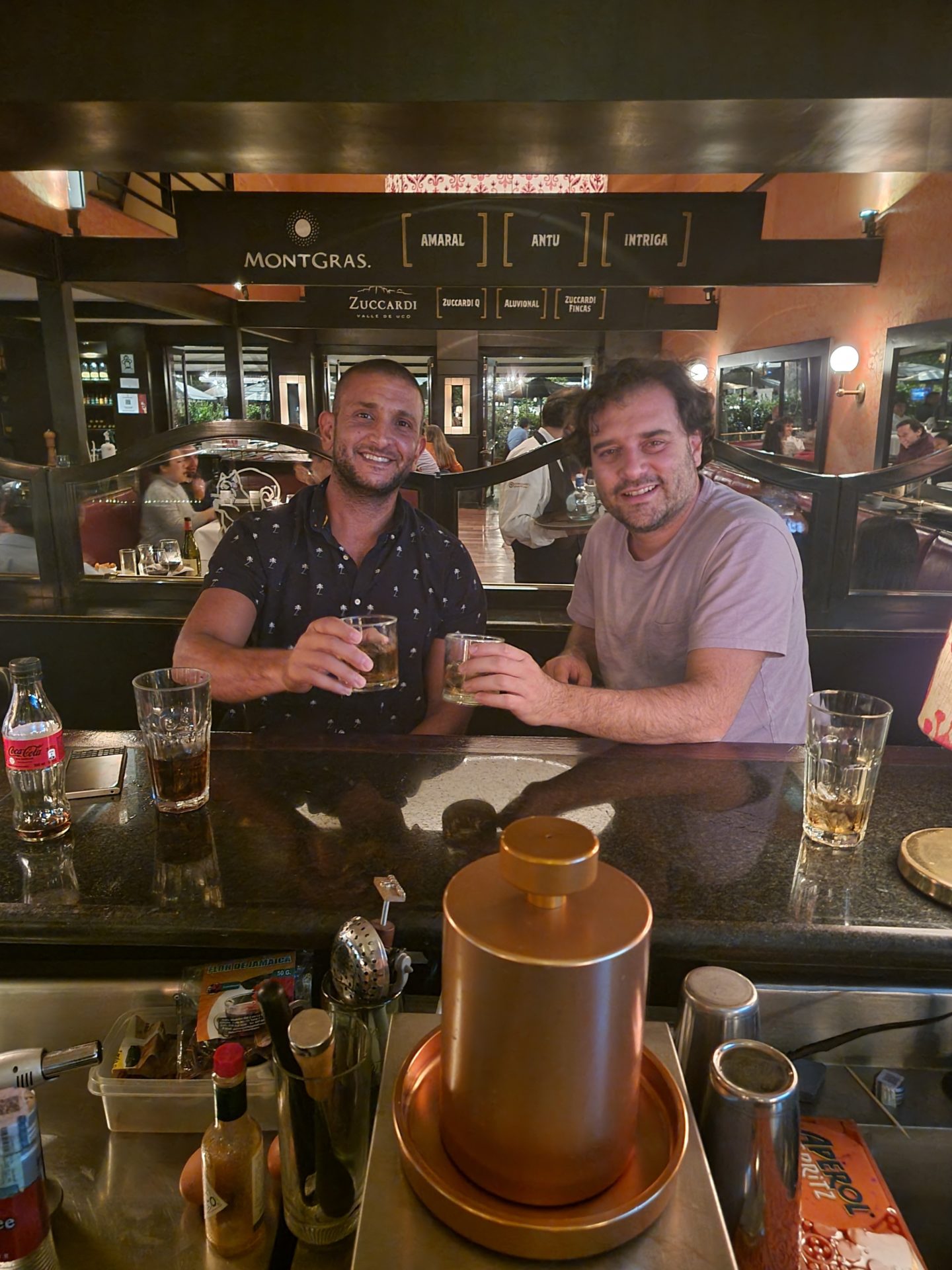 two men sitting at a bar with drinks