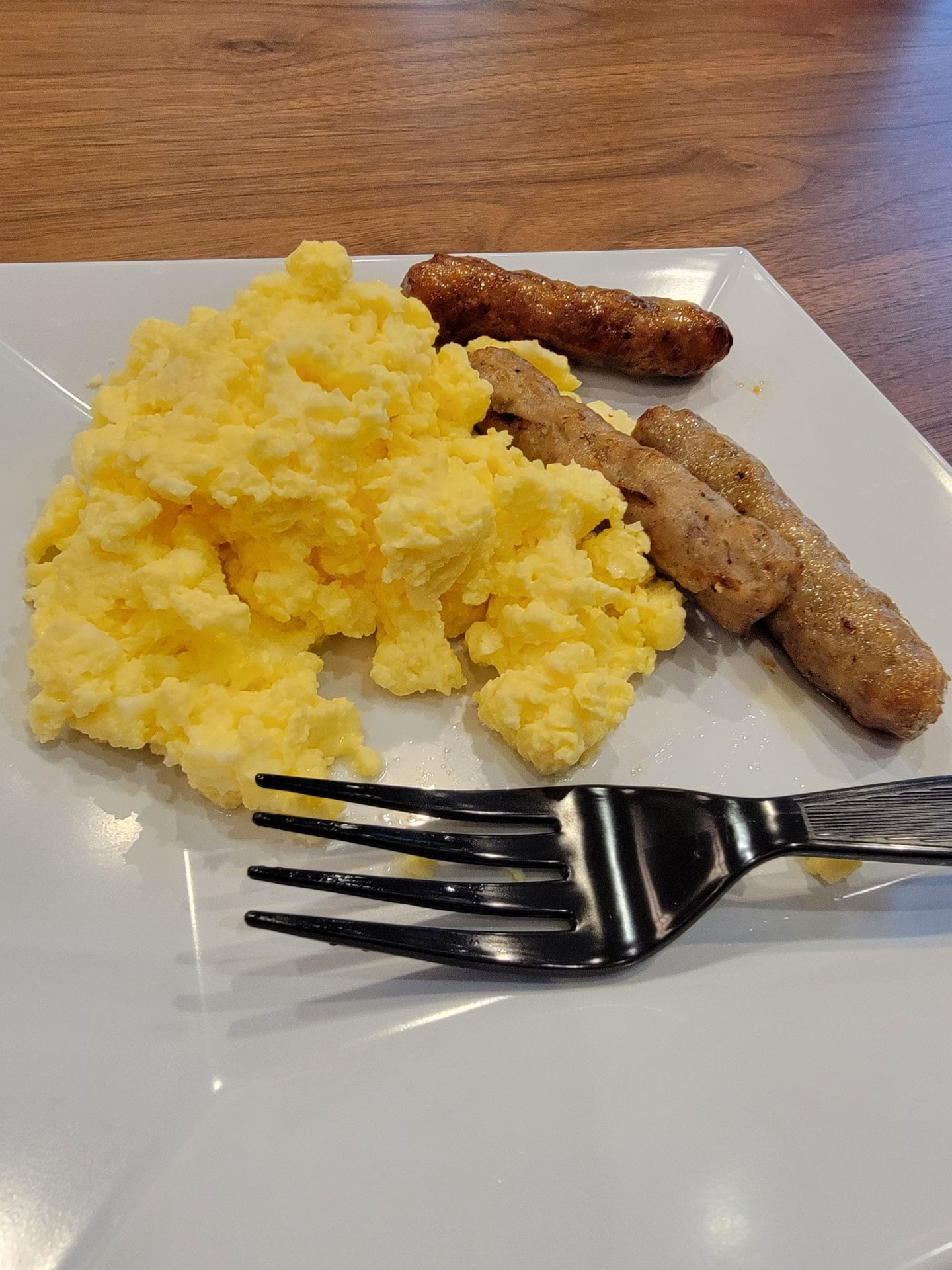 a plate of scrambled eggs sausages and a fork