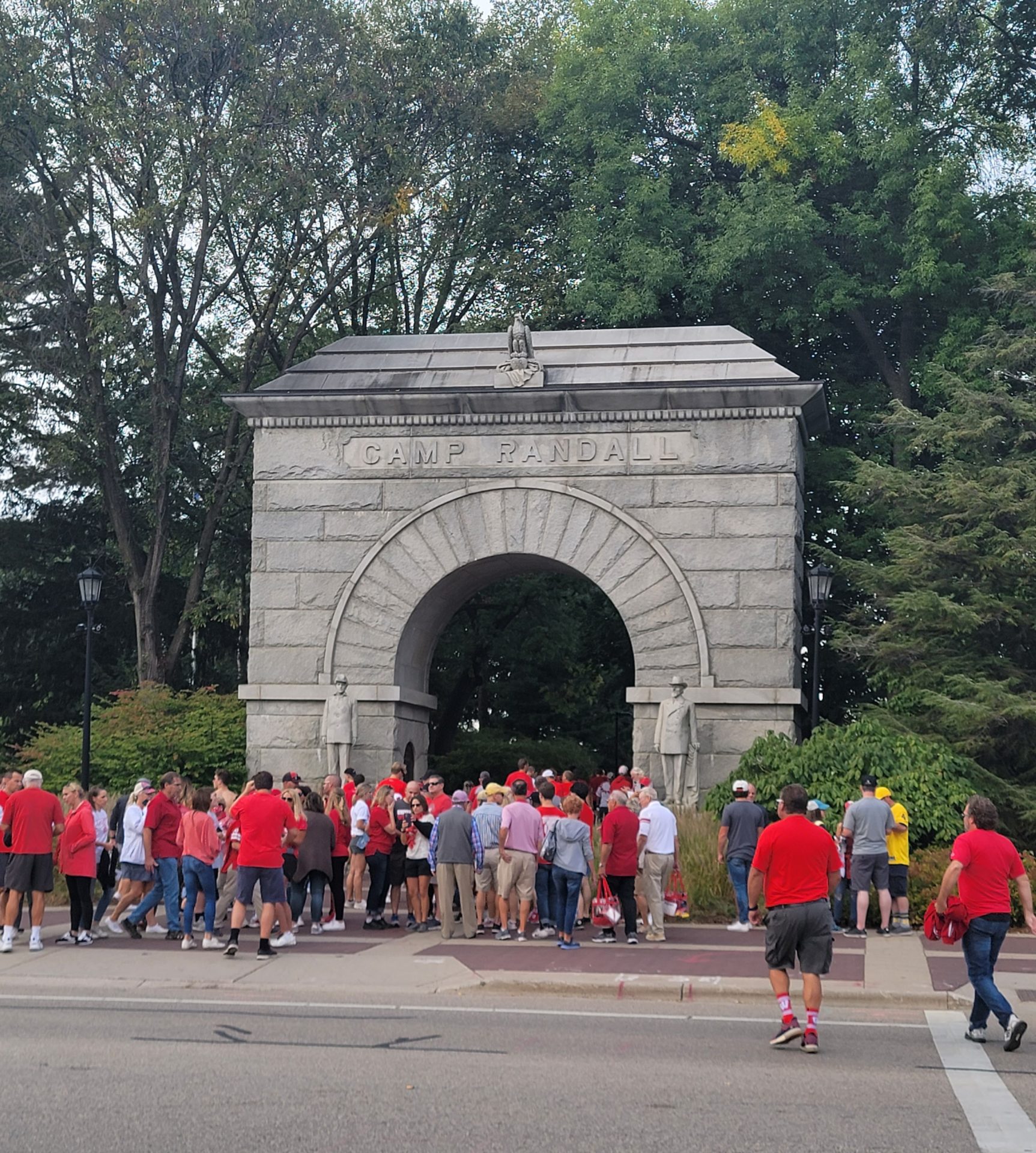 a group of people standing in front of a stone archway with Camp Randall Stadium in the background