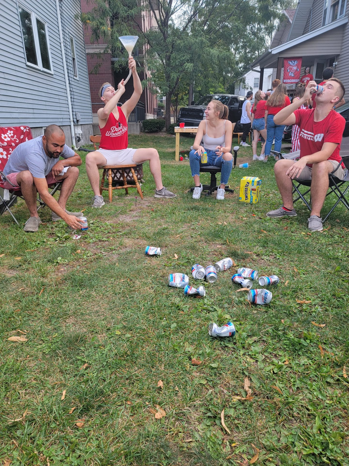 a group of people sitting on chairs in a yard with cans in the middle