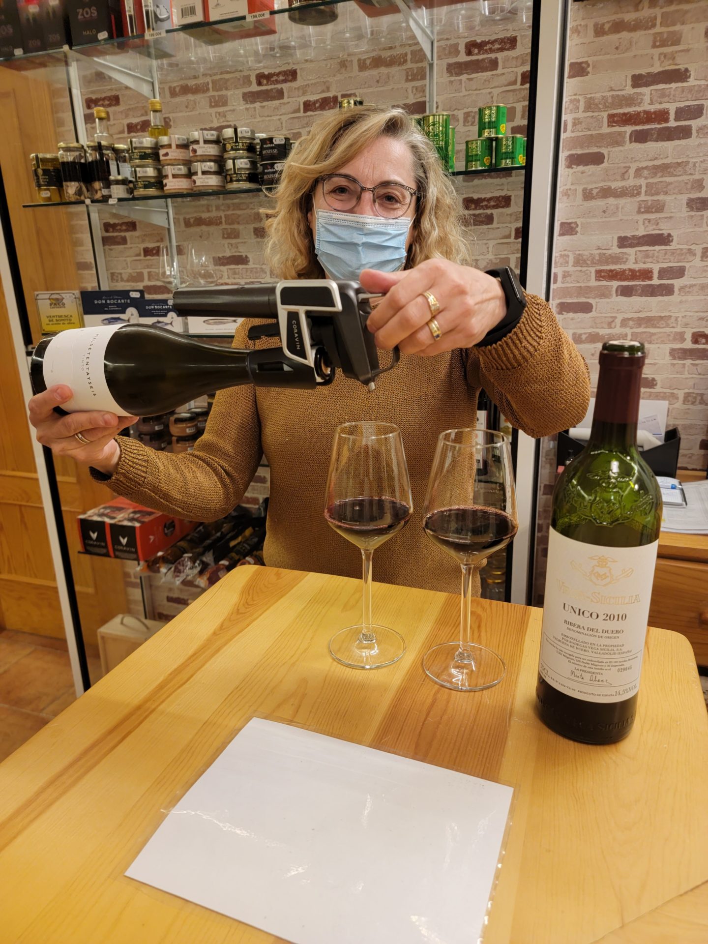 a woman wearing a face mask holding a wine bottle and glasses