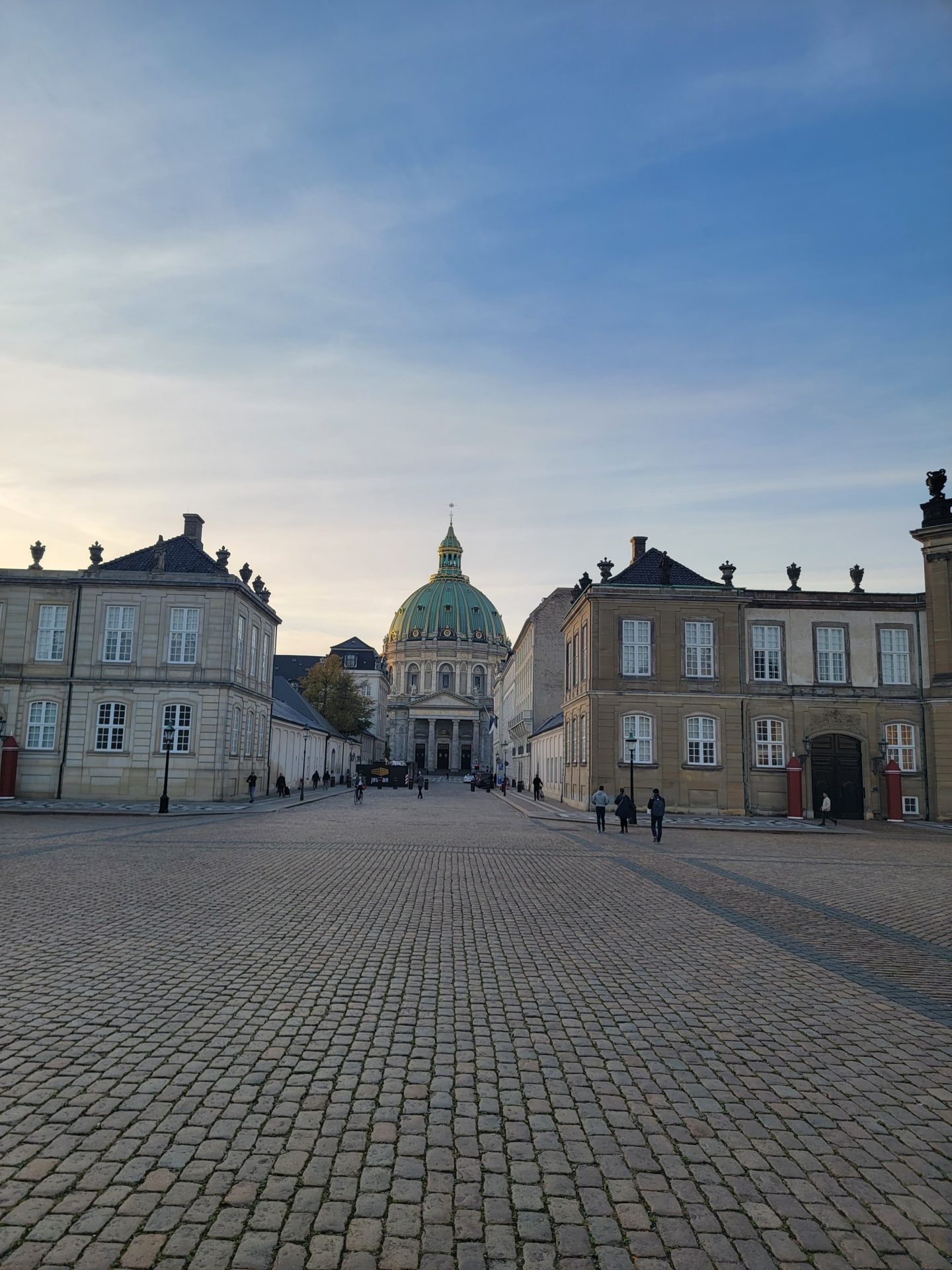 a stone street with buildings and a dome with Amalienborg in the background