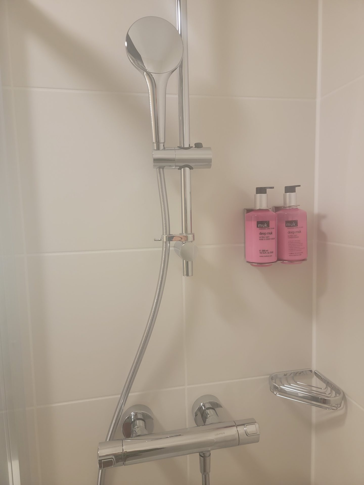 a shower head and faucet with pink bottles of shampoo