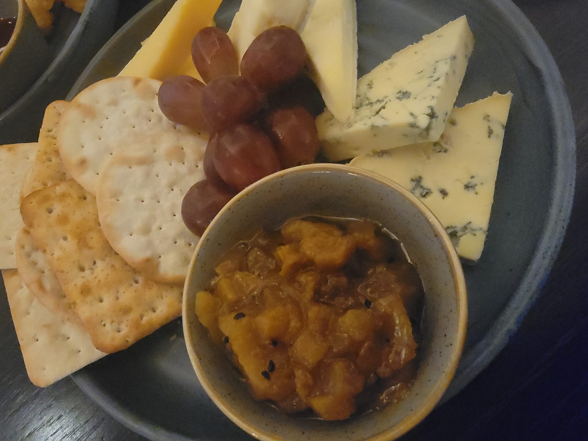 a plate of cheese and crackers with grapes and jam