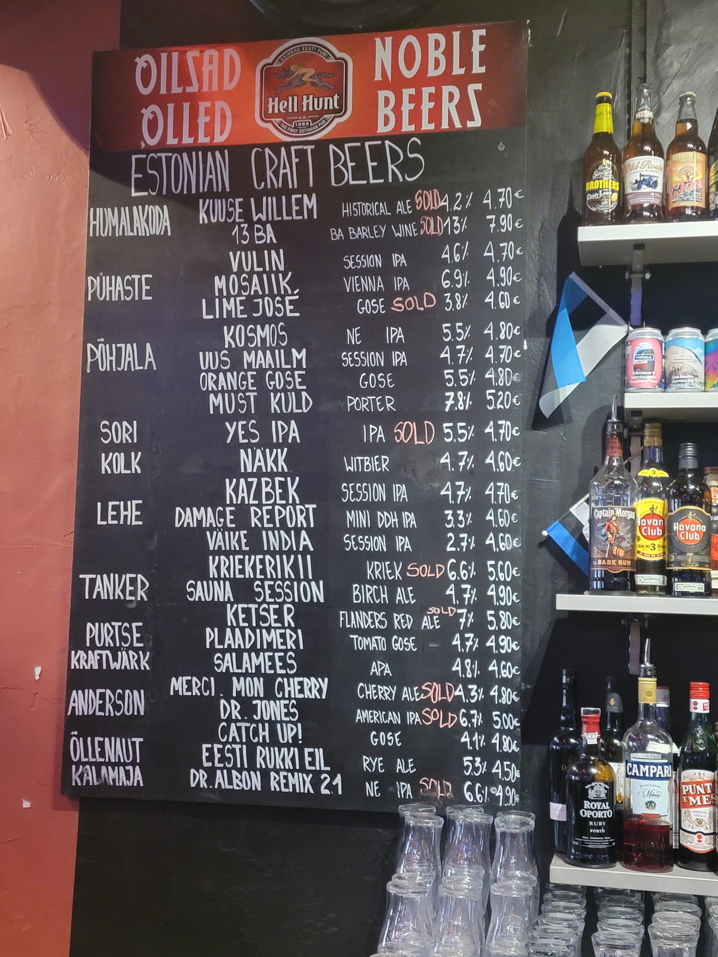 a black board with white text and bottles of alcohol on the wall