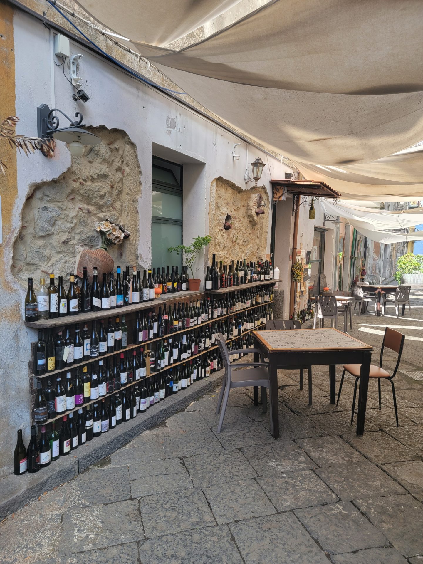 a table and chairs outside a building with a wall of bottles