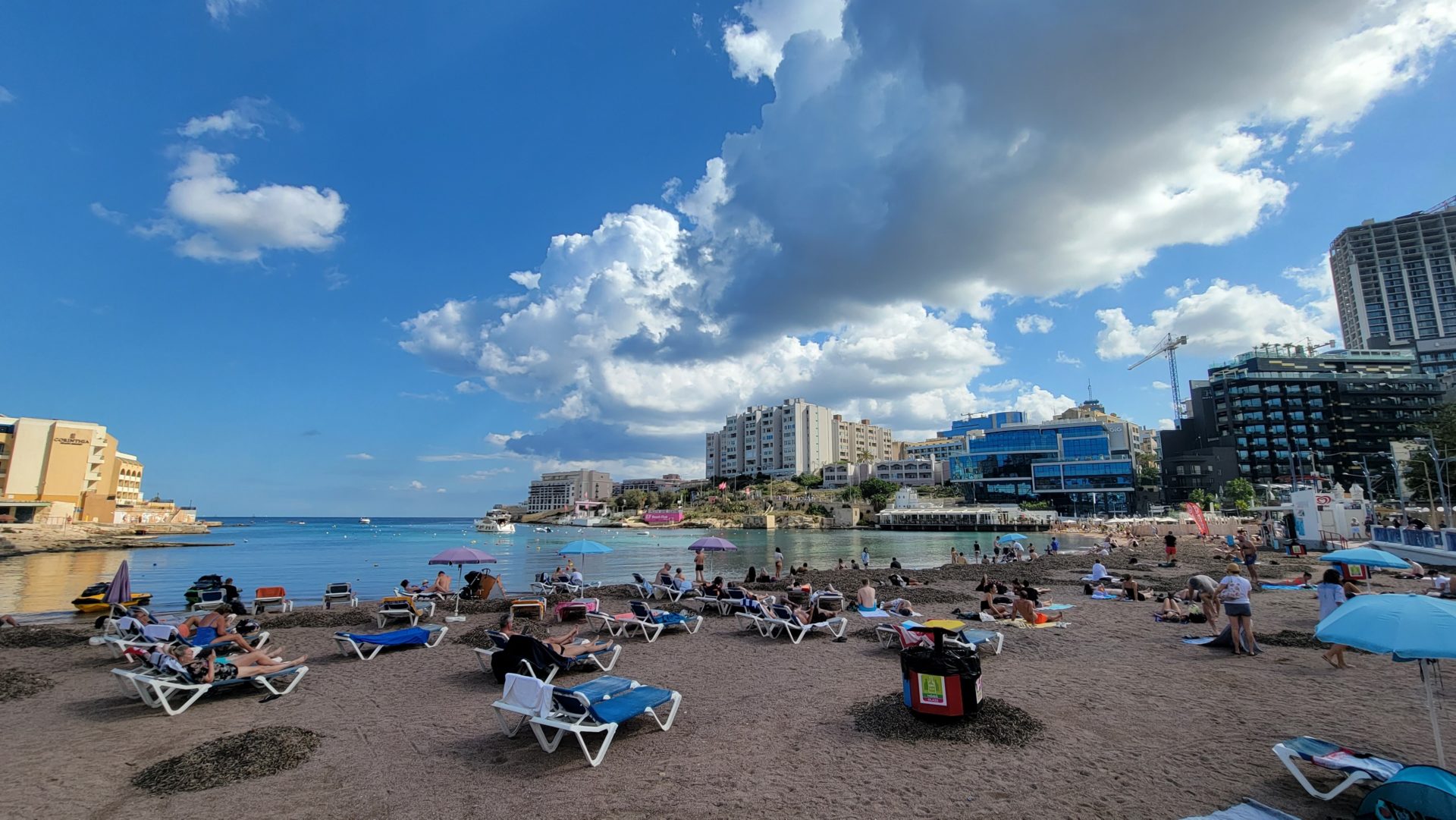 a beach with chairs and umbrellas and buildings in the background