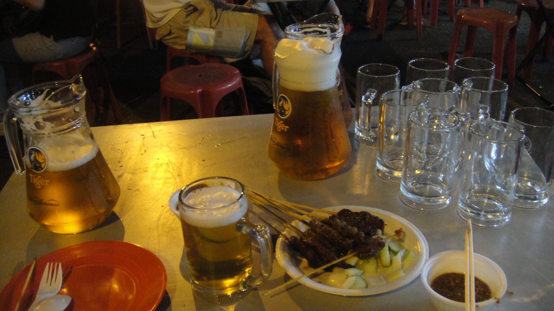 a plate of meat and vegetables on a table with glasses and a pitcher of beer