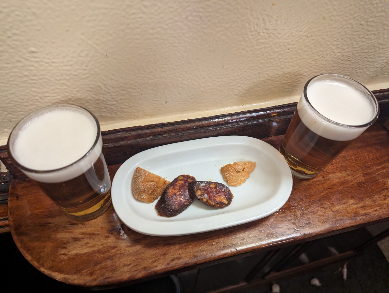 a plate of food and two glasses of beer on a wooden surface