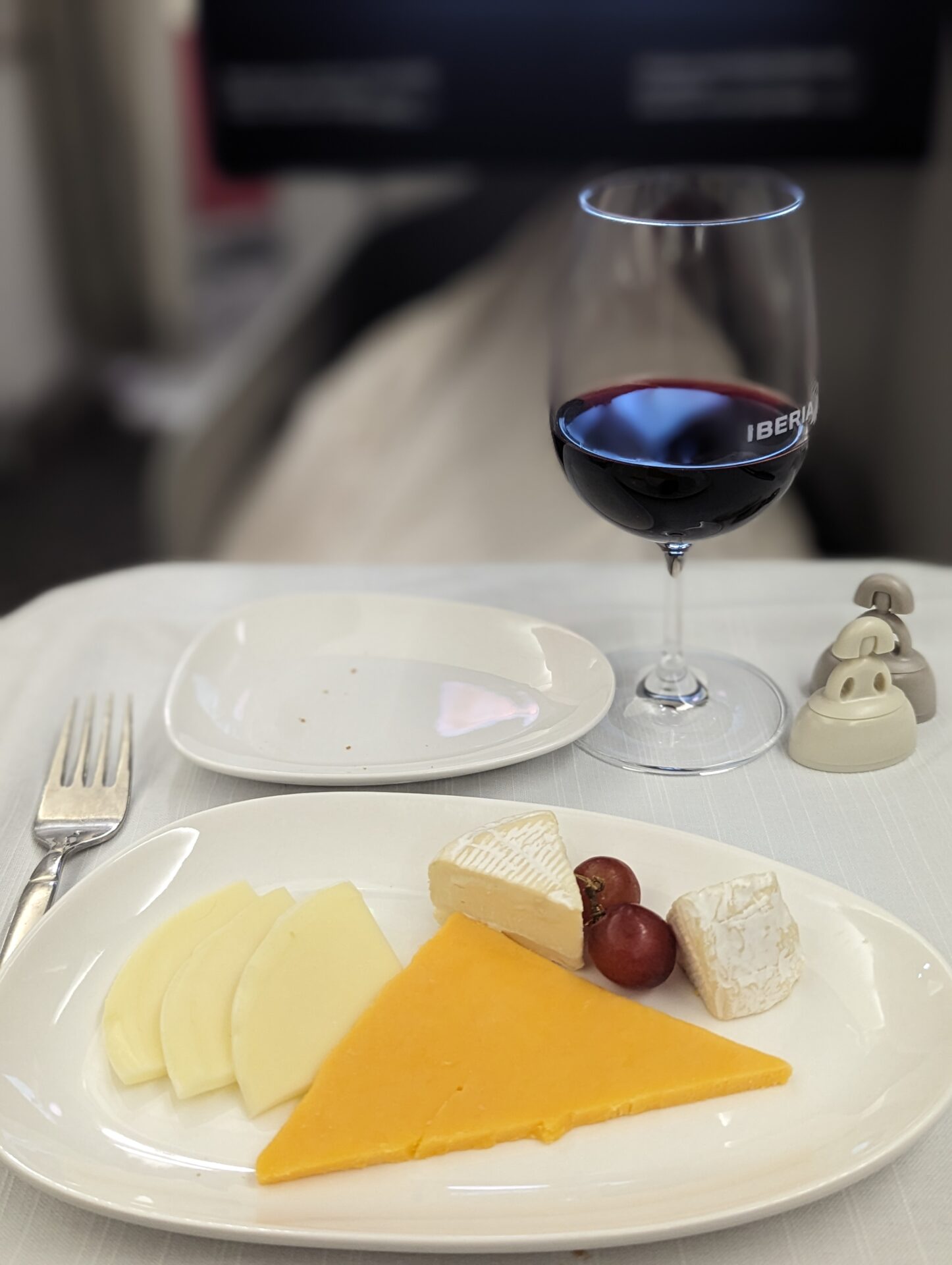 a plate of cheese and grapes on a table with a glass of wine