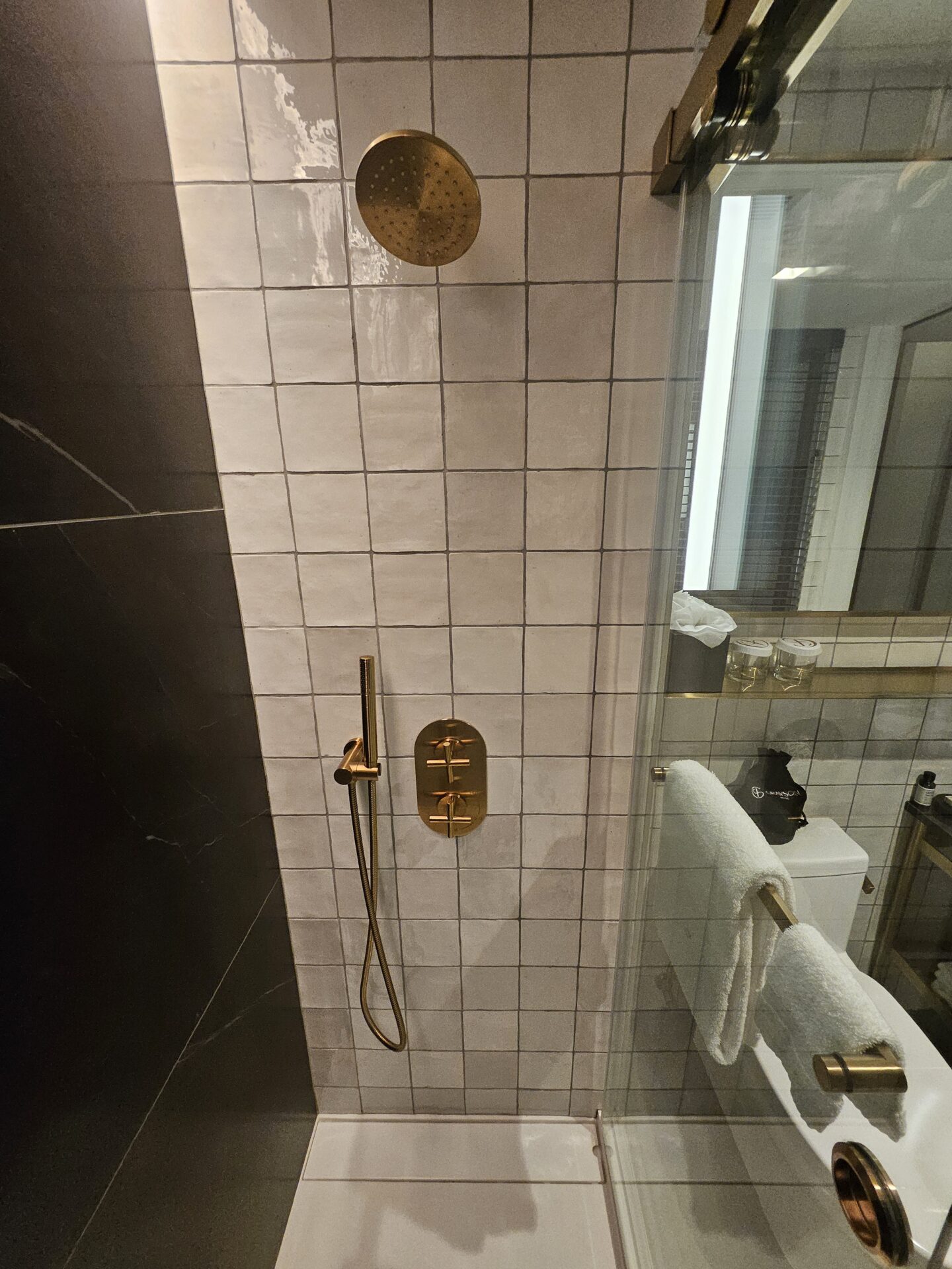 a shower with a gold faucet and a white towel on a rack