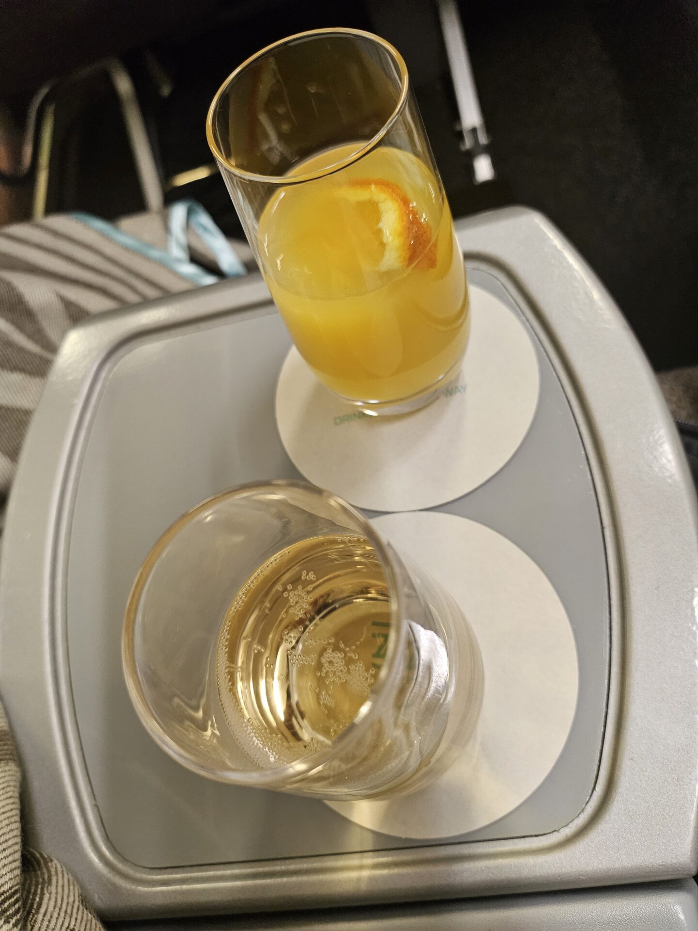 a glass of orange juice and a glass of liquid on a tray