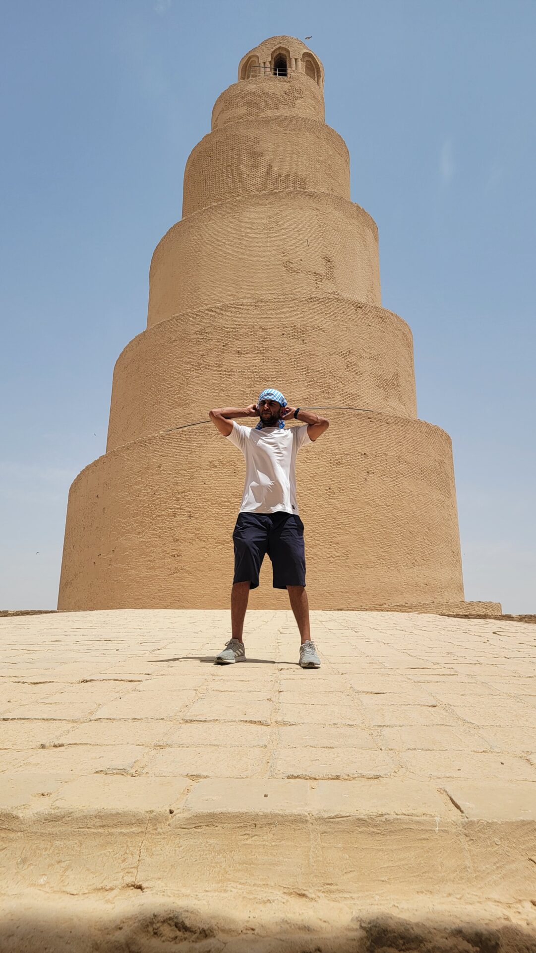 a man standing in front of a large tower with Great Mosque of Samarra in the background