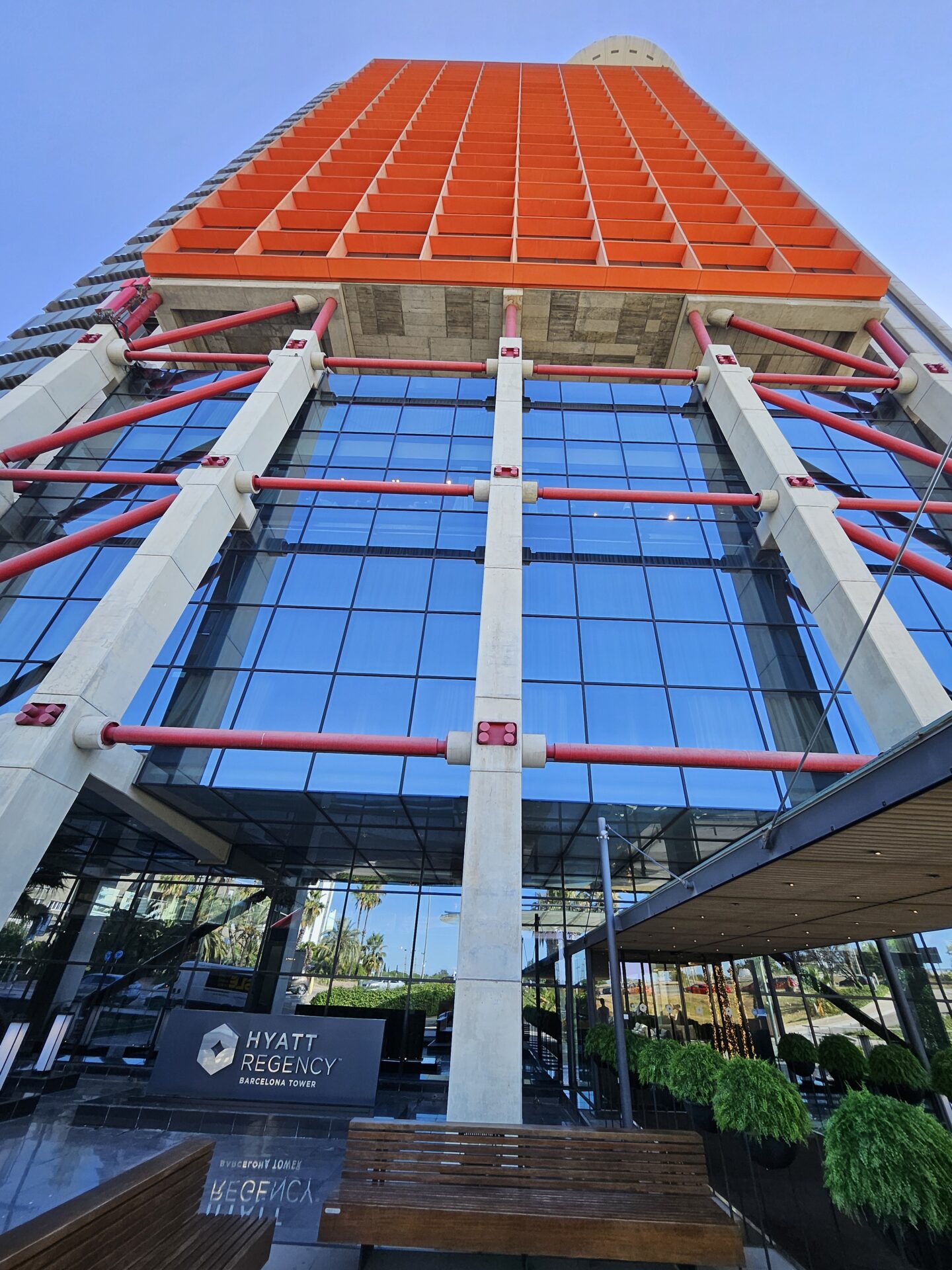 a tall building with glass walls and a red and orange structure