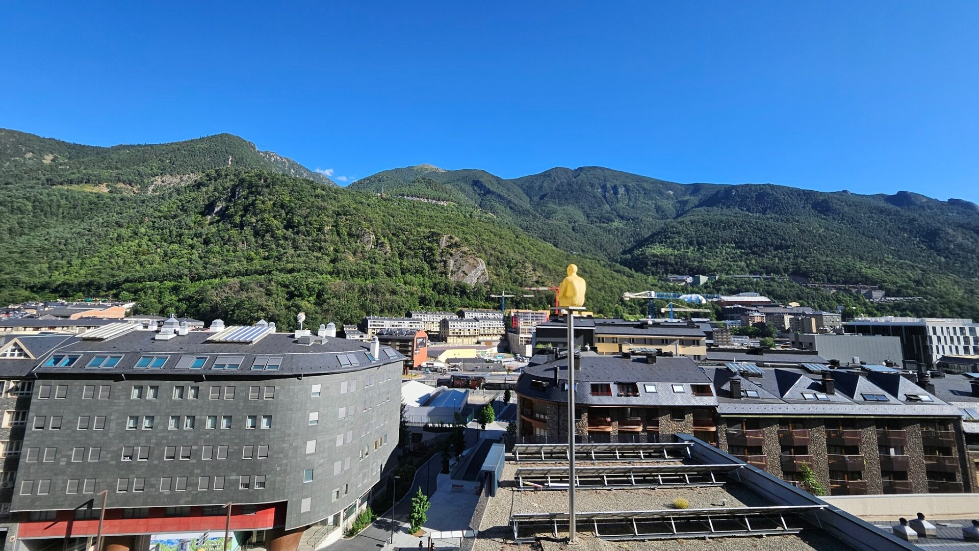 a yellow statue on top of a building with mountains in the background