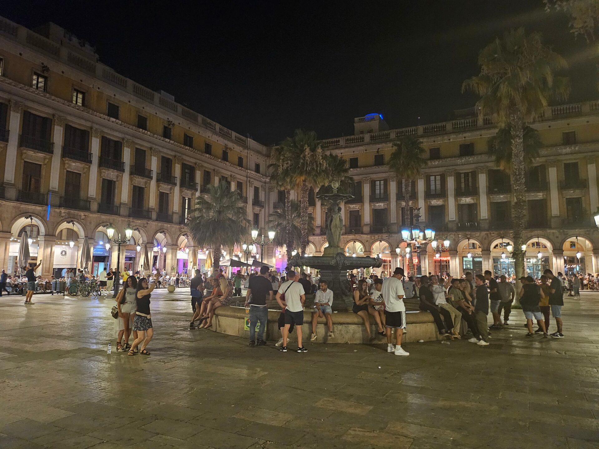 a group of people in a plaza with a fountain in front of a building