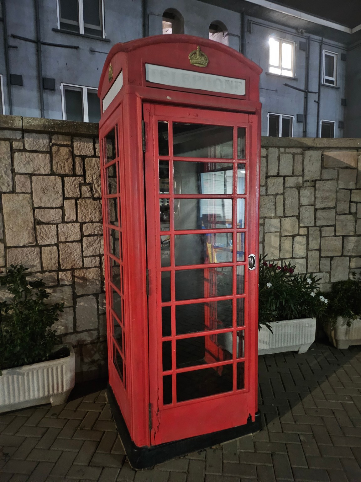 a red telephone booth in front of a stone wall