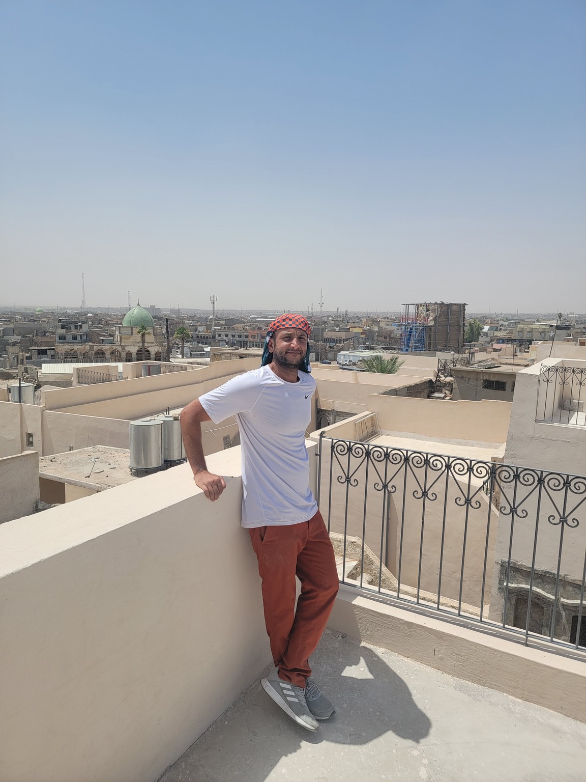 a man standing on a balcony with a fence and a city in the background