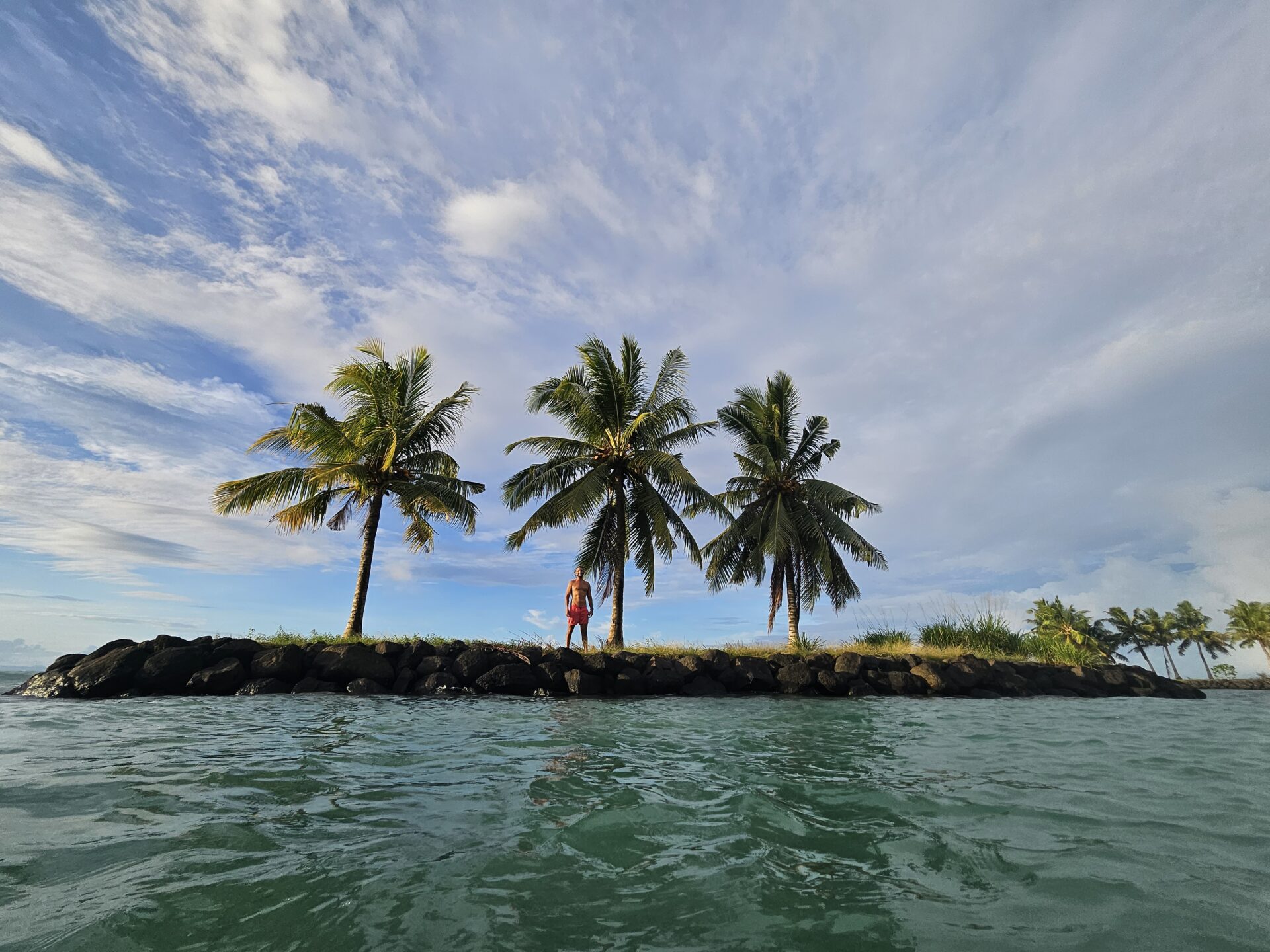 a woman standing on a rocky island with palm trees